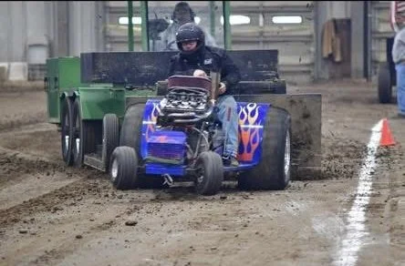 Person driving a small, blue, race-style go-kart on a dirt track indoors.