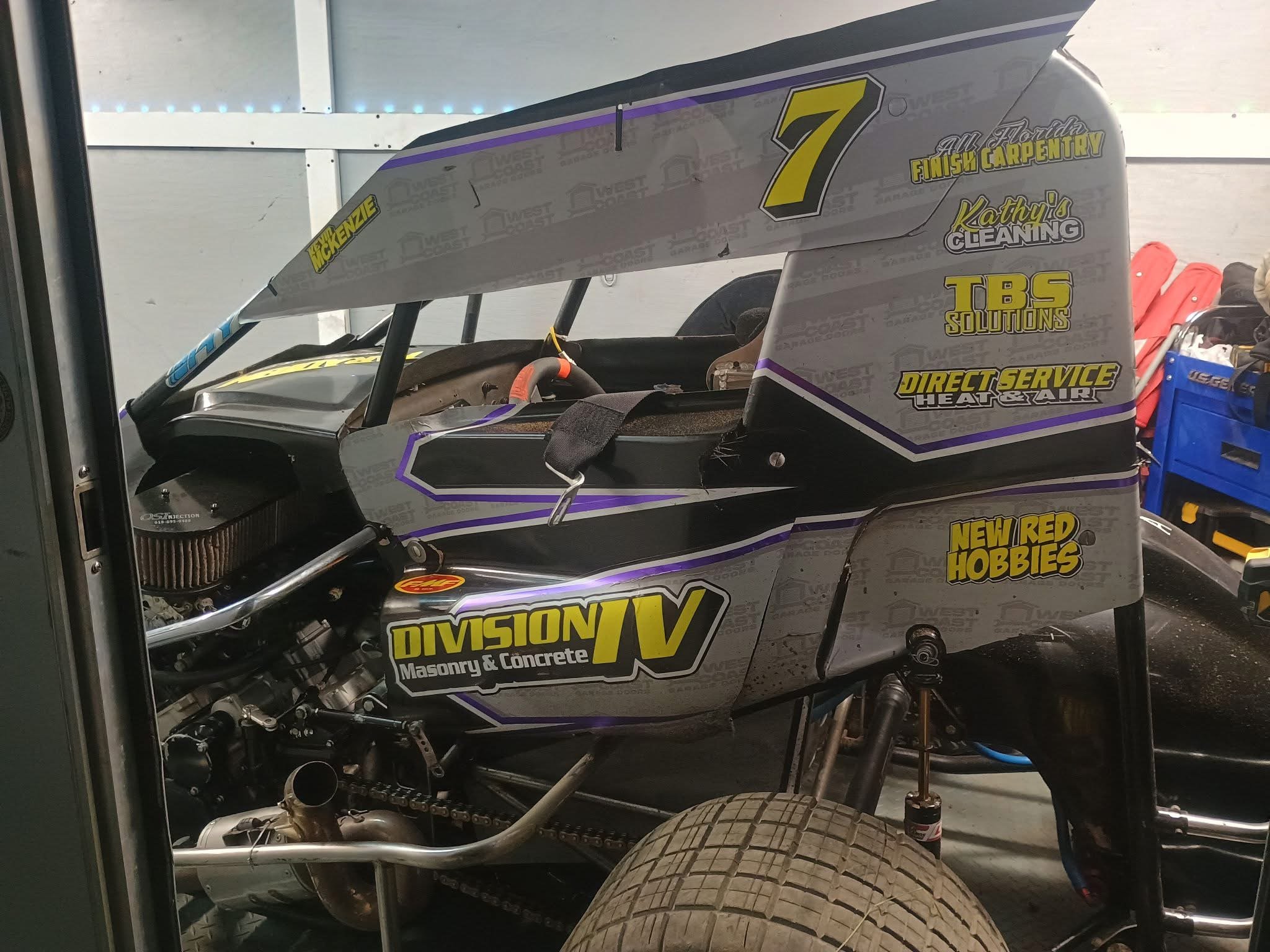 Race car with various sponsor logos and a large rear spoiler, partially visible, in a garage setting.
