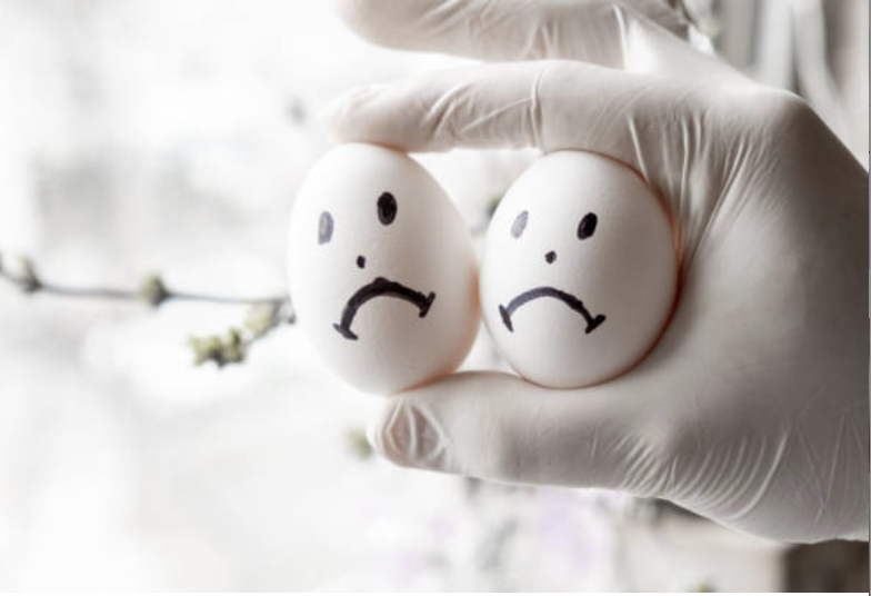 Two eggs with sad face drawn on them being held in a gloved hand.