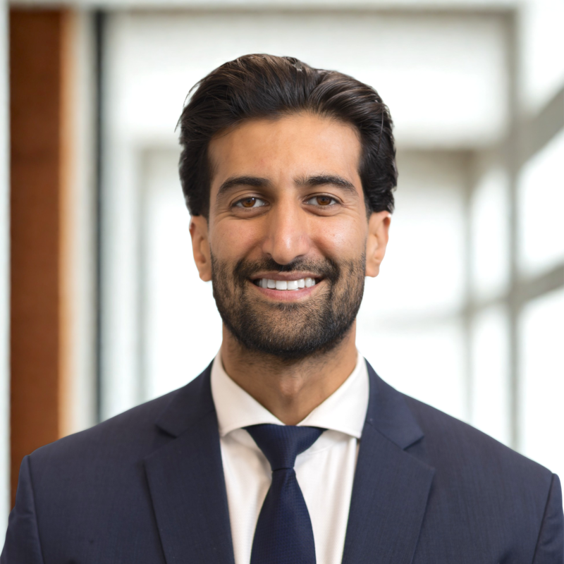 Professional headshot of a man with dark hair, beard, and a friendly smile, wearing a suit jacket, white shirt, and red tie.