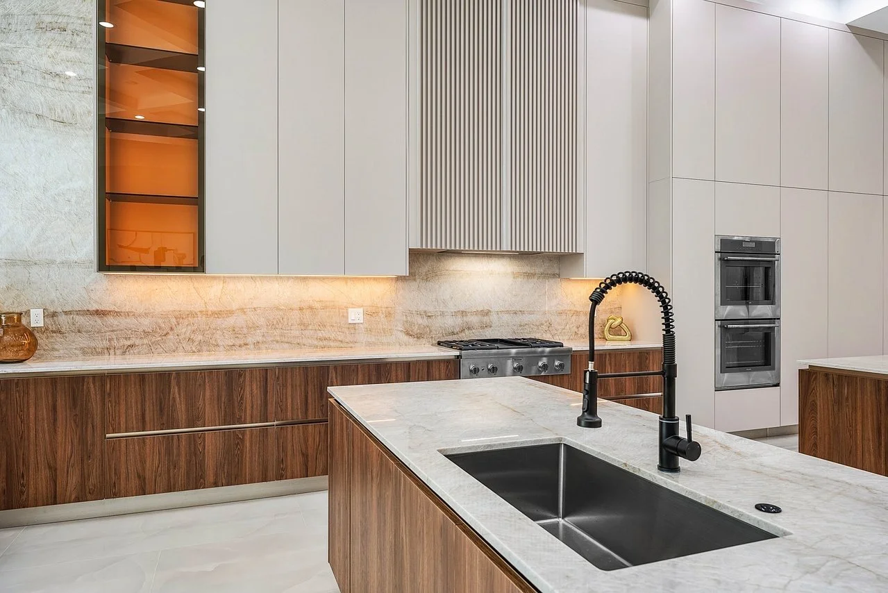 Modern kitchen with white upper cabinets, wooden lower cabinets, marble countertops, a black sink with a black gooseneck faucet, and stainless steel appliances.
