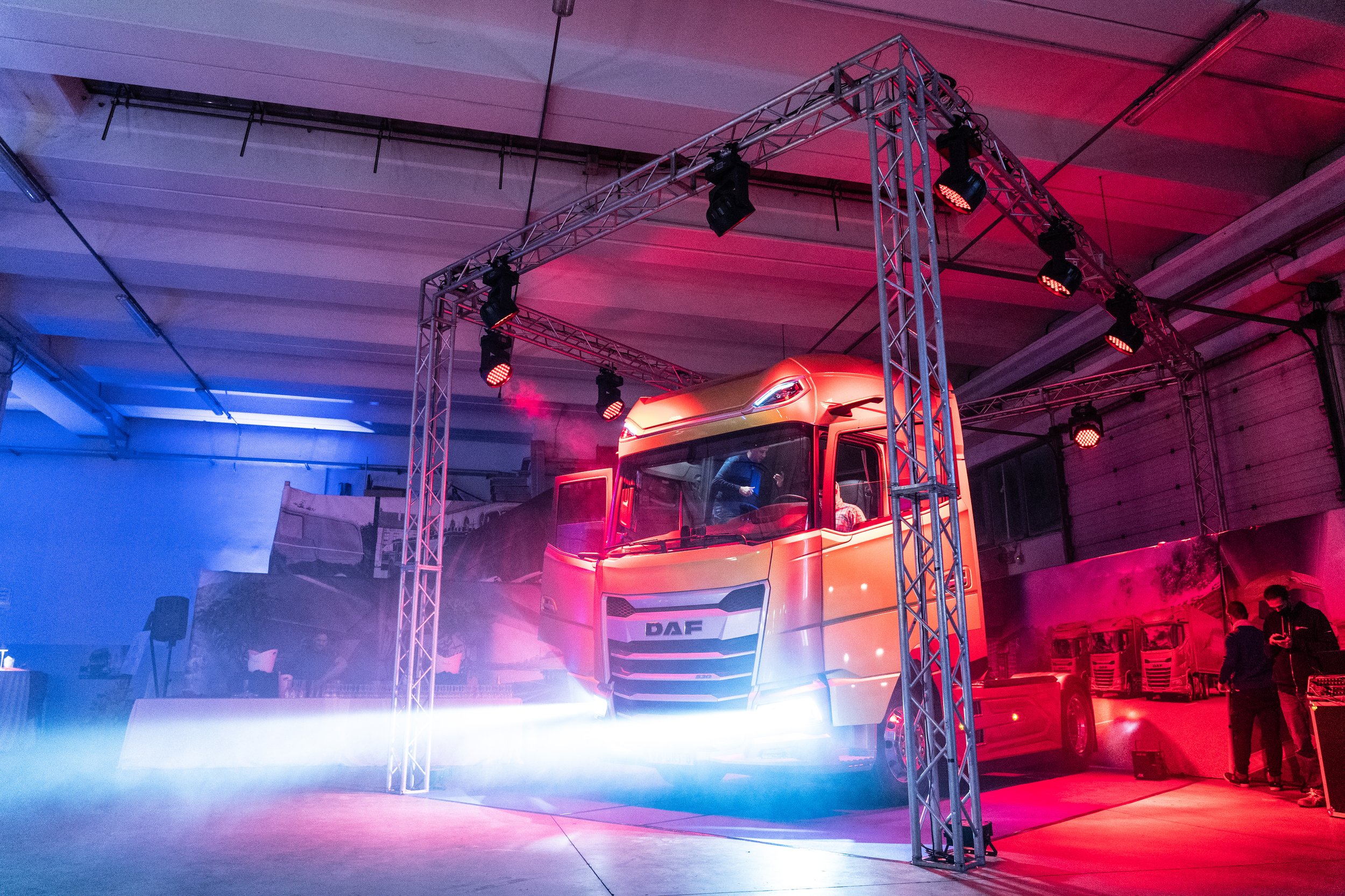 Camion DAF presentato in un evento con luci colorate rosa, blu e bianche, in un ambiente indoor.