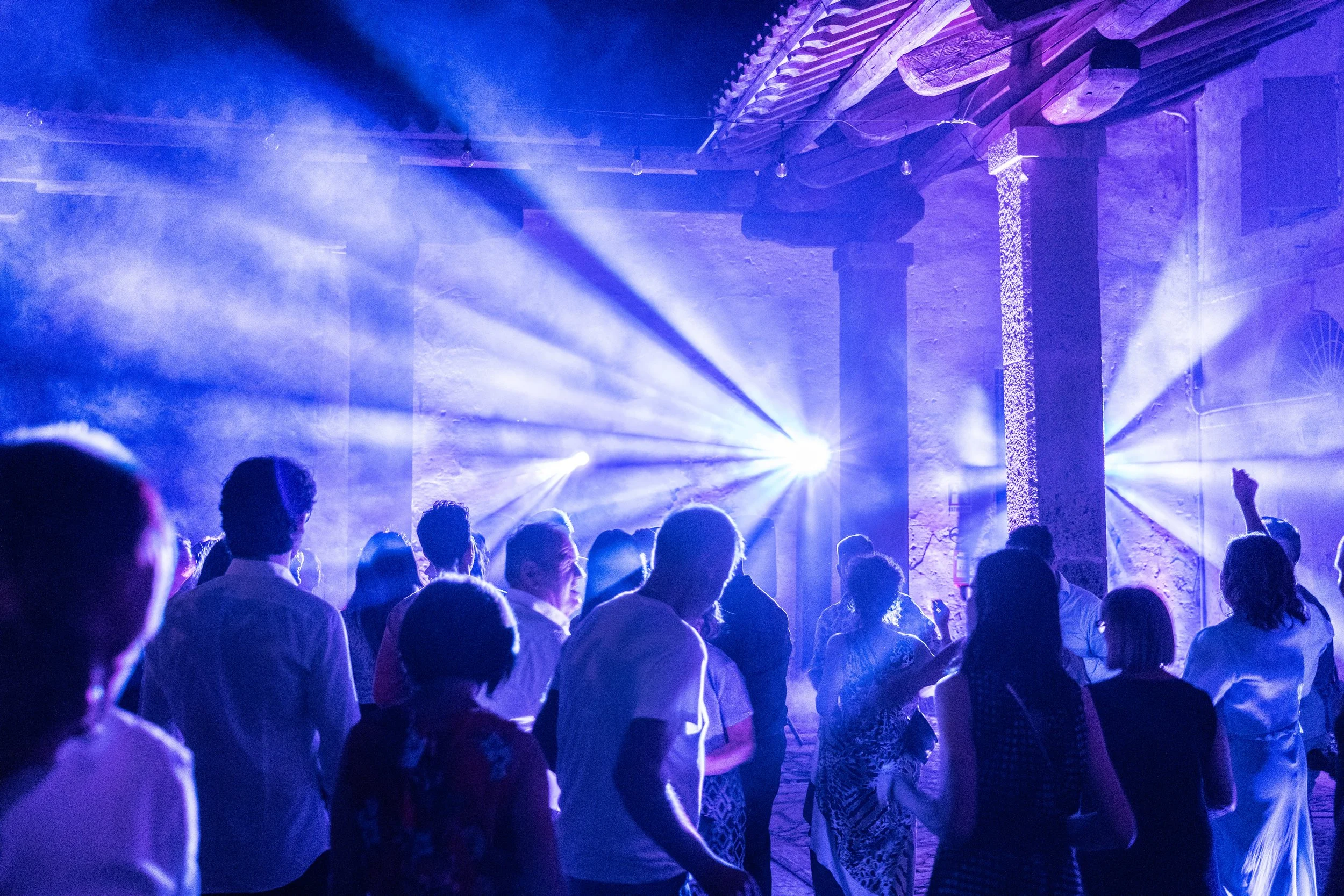 Gruppo di persone che danzano in una sala illuminate da luci blu e fumogeni.