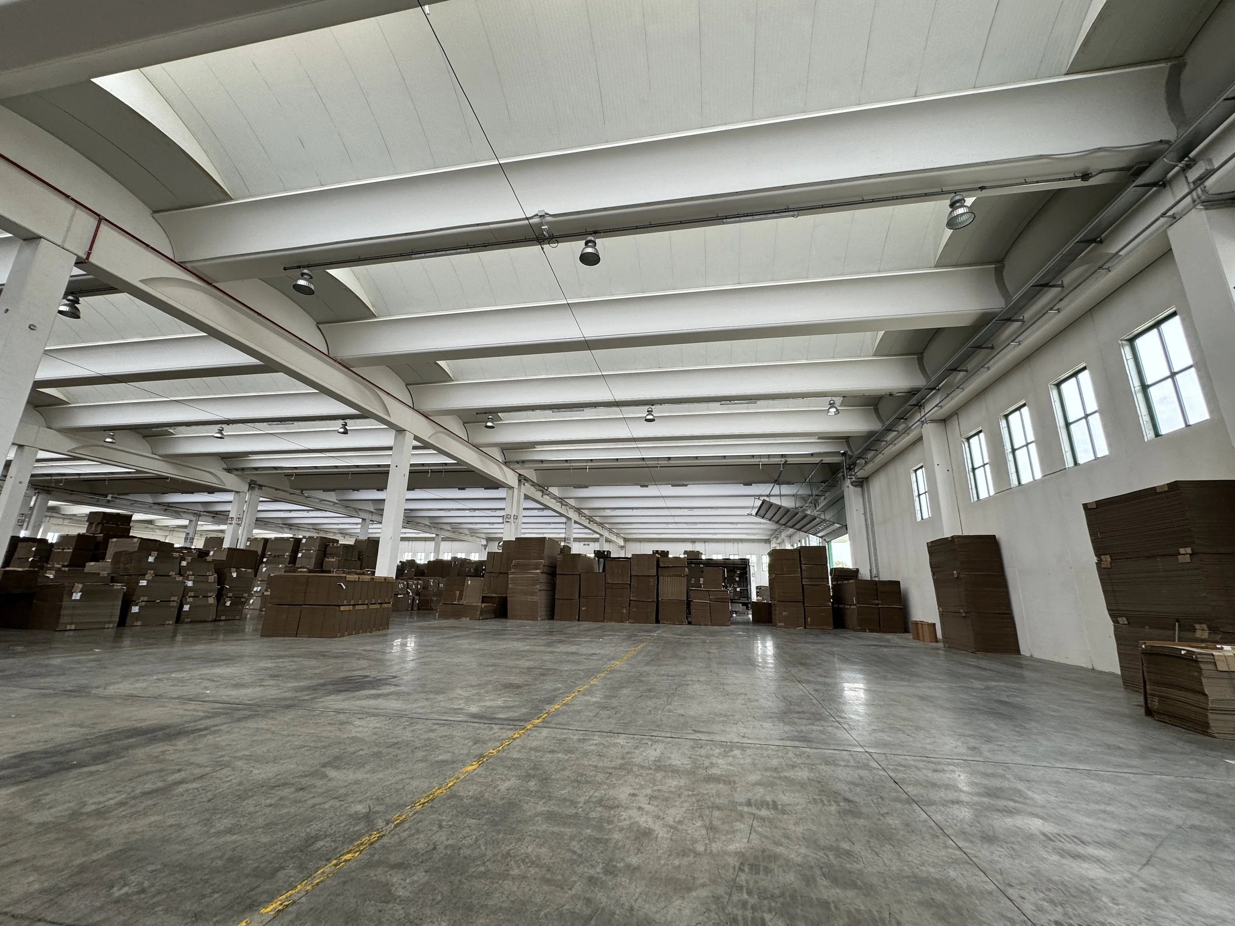 Interno di un magazzino con scaffali pieni di cartoni e un pavimento in cemento lucido.