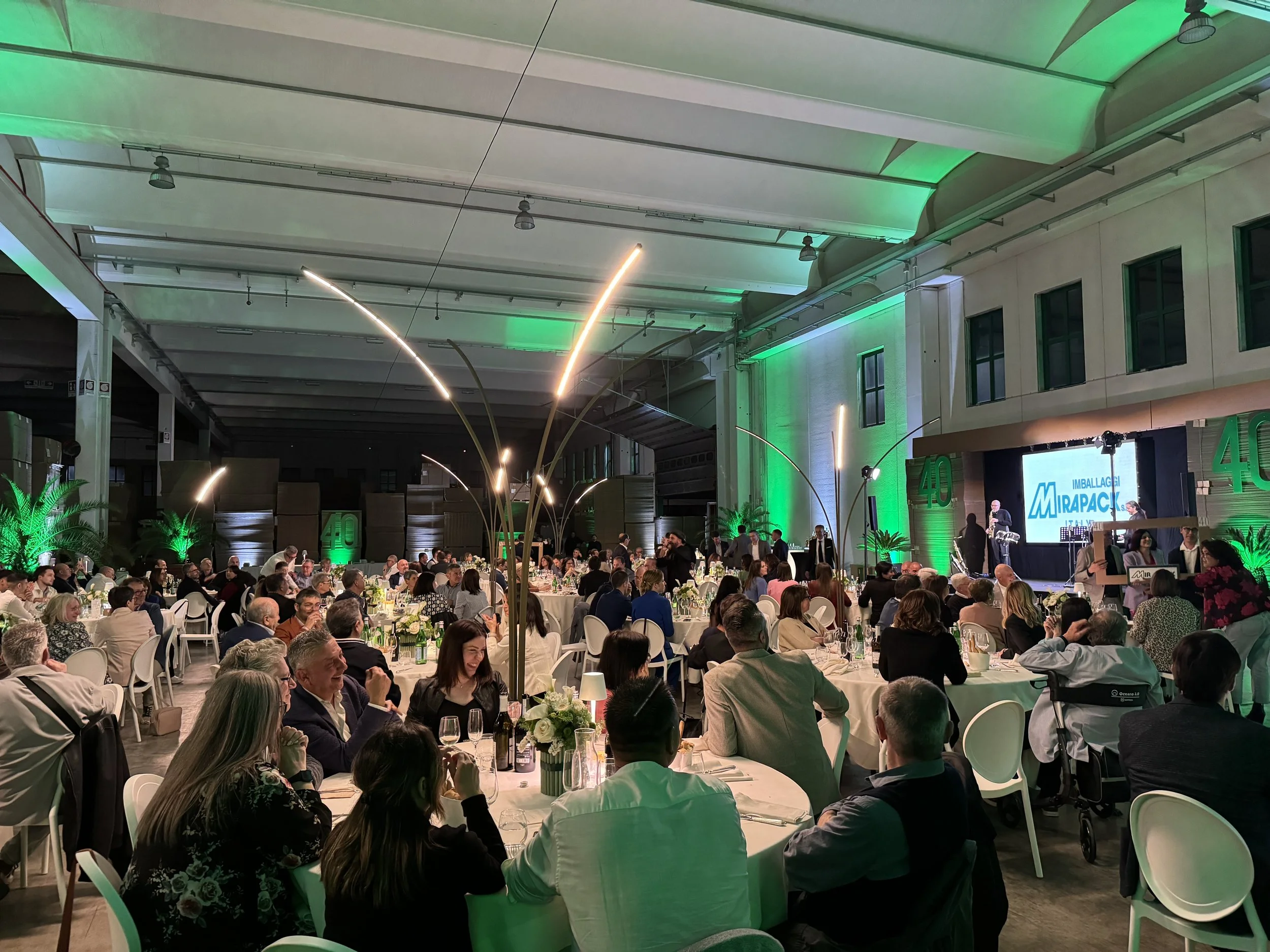 Evento aziendale con molte persone sedute a tavoli rotondi in un grande spazio con illuminazione verde e decorazioni natalizie.