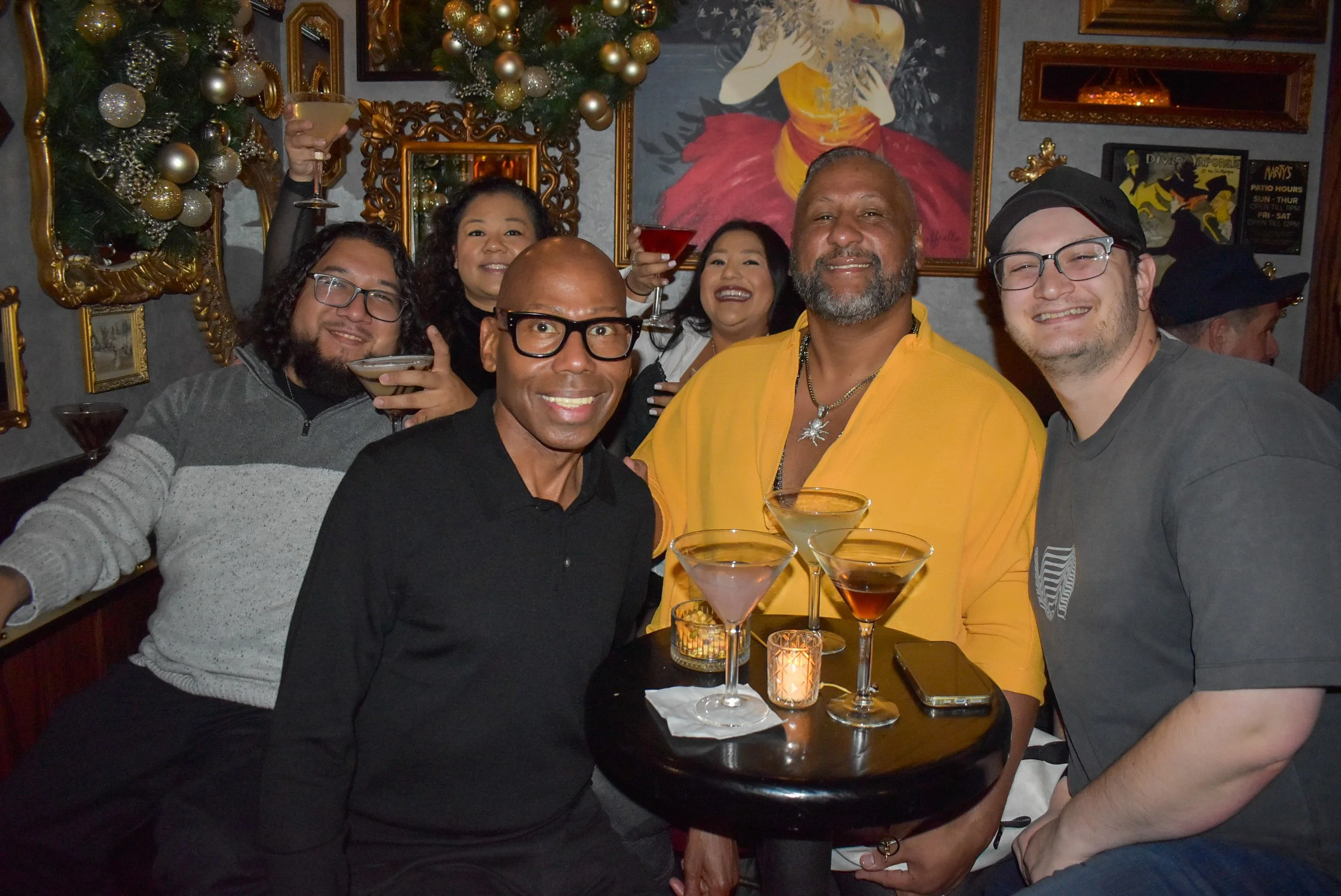 A group of customers are holding up their martini glasses and posing for a photo