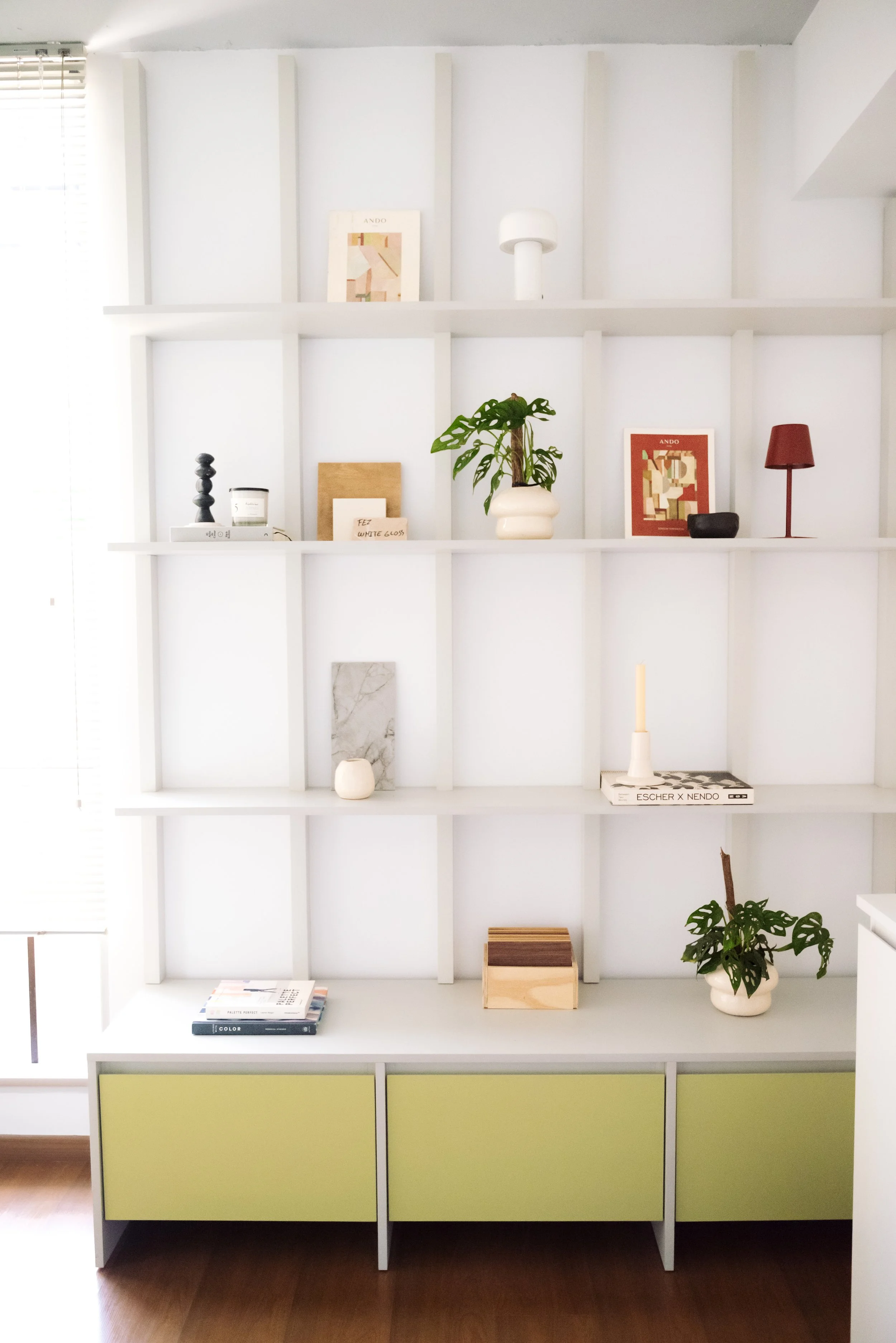 White bookshelf with decorative items, books, and potted plants, with green storage compartments at the bottom.