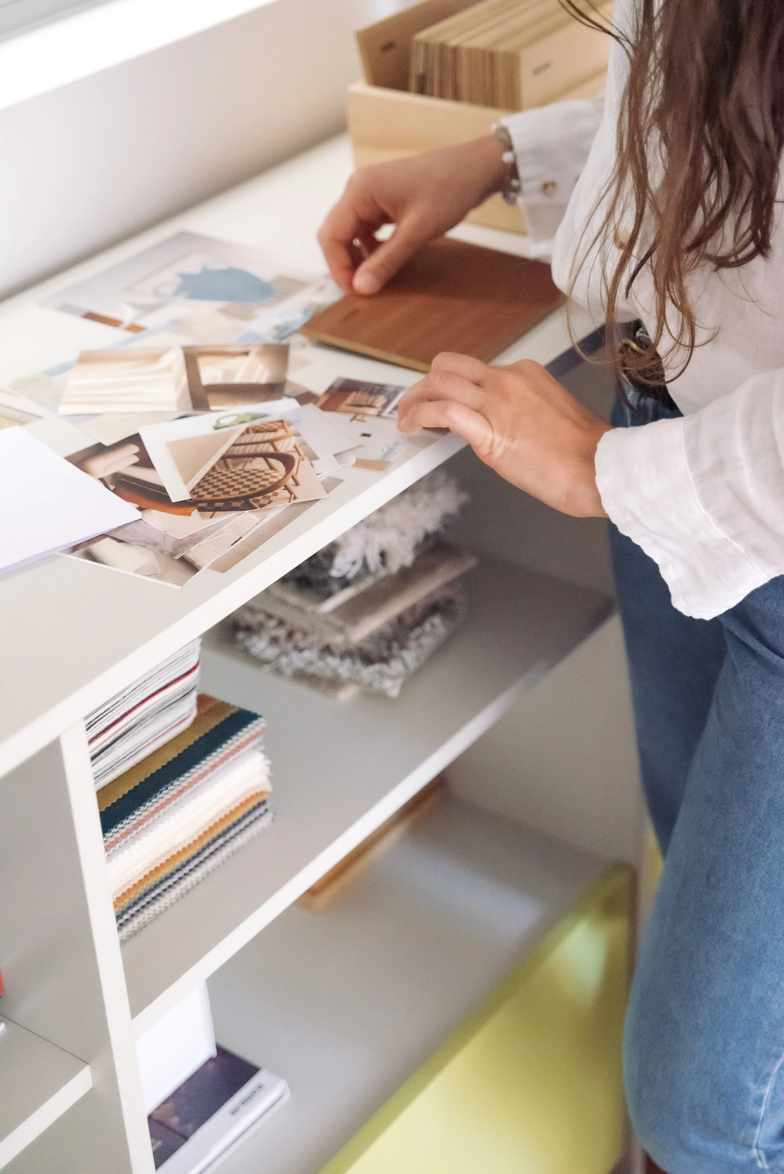 Person looking at fabric and color samples on a white shelf, working on interior design or decorating project.