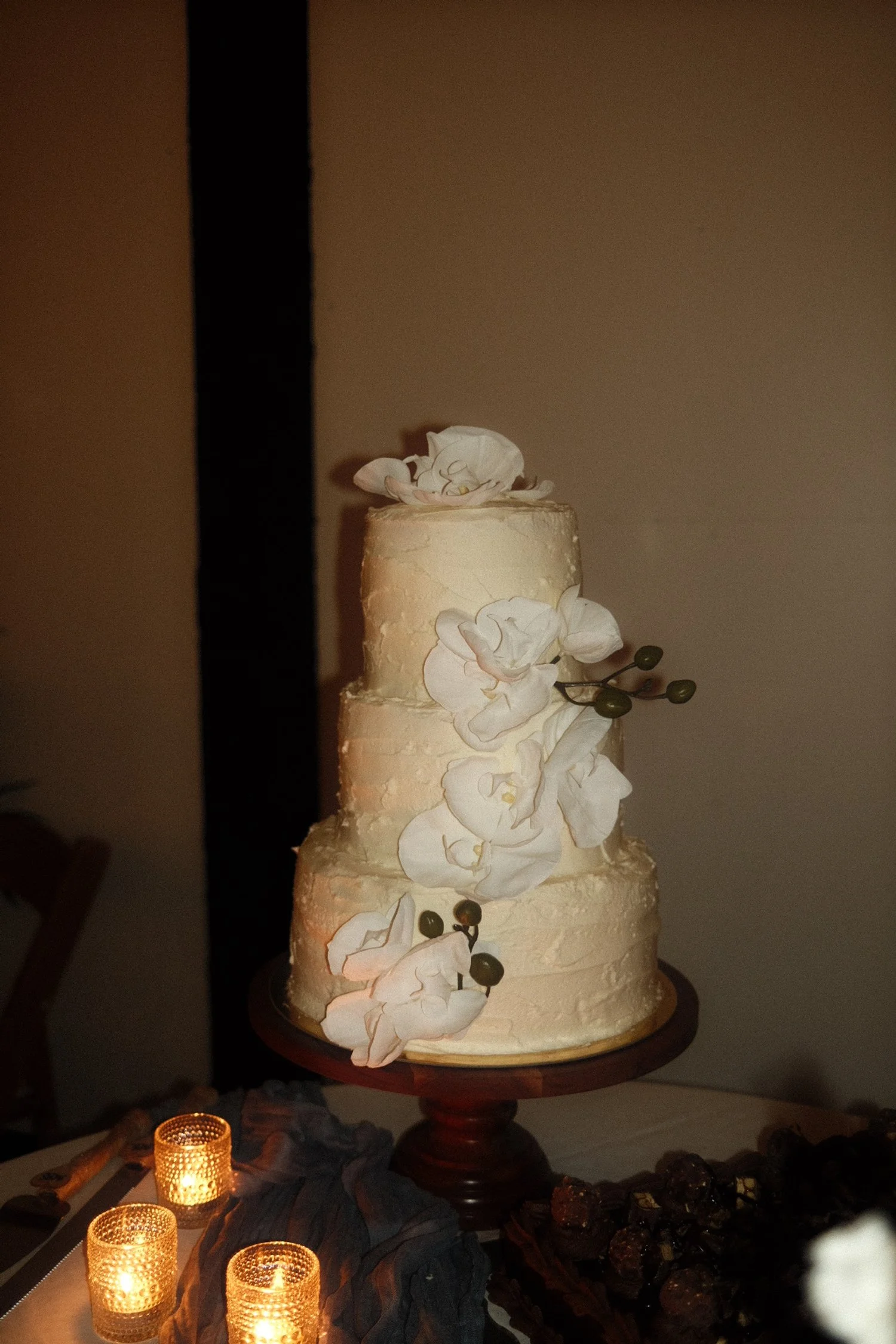 A three-tier white wedding cake decorated with edible white orchids and green stems, placed on a wooden cake stand.