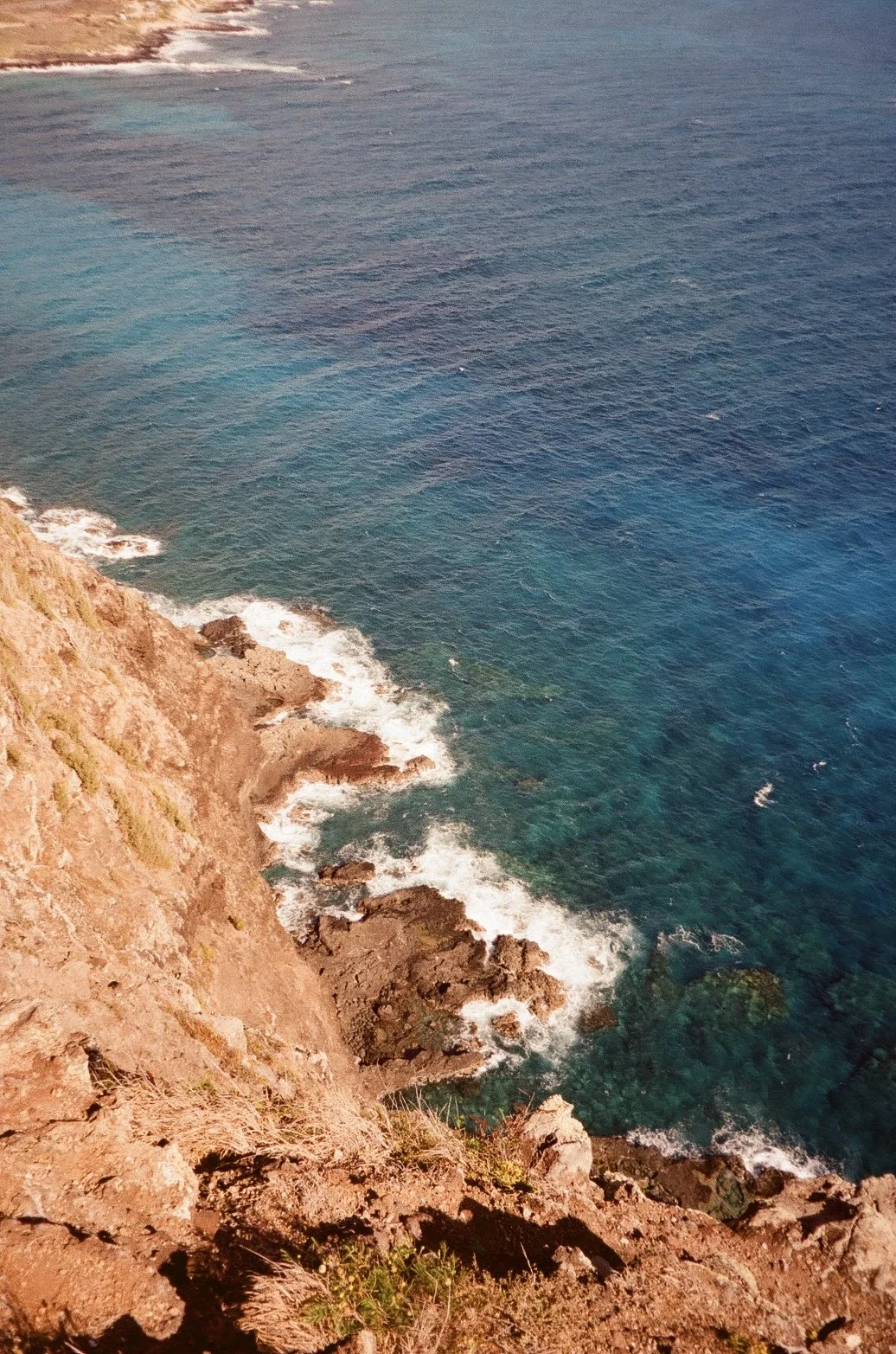 Aerial view of a rugged coastal cliff with rocky shoreline and clear blue ocean water.