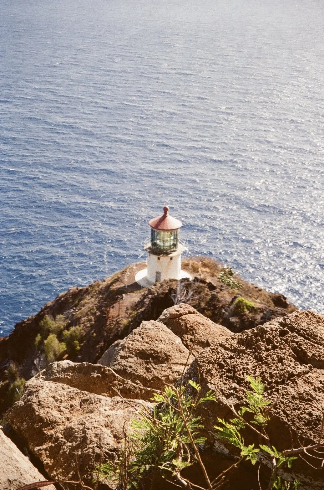 A lighthouse on a rocky cliff overlooking the ocean with a bright, sunny sky.