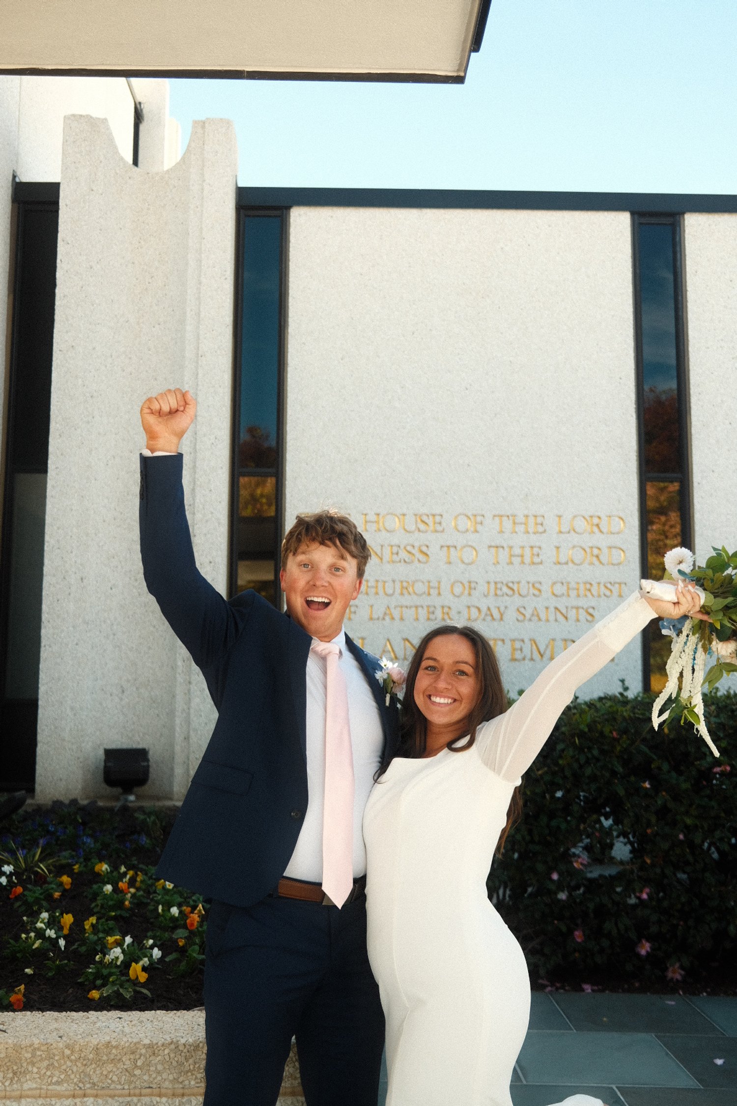 Happy bride and groom celebrating in front of a church after wedding, with arms raised and smiling.