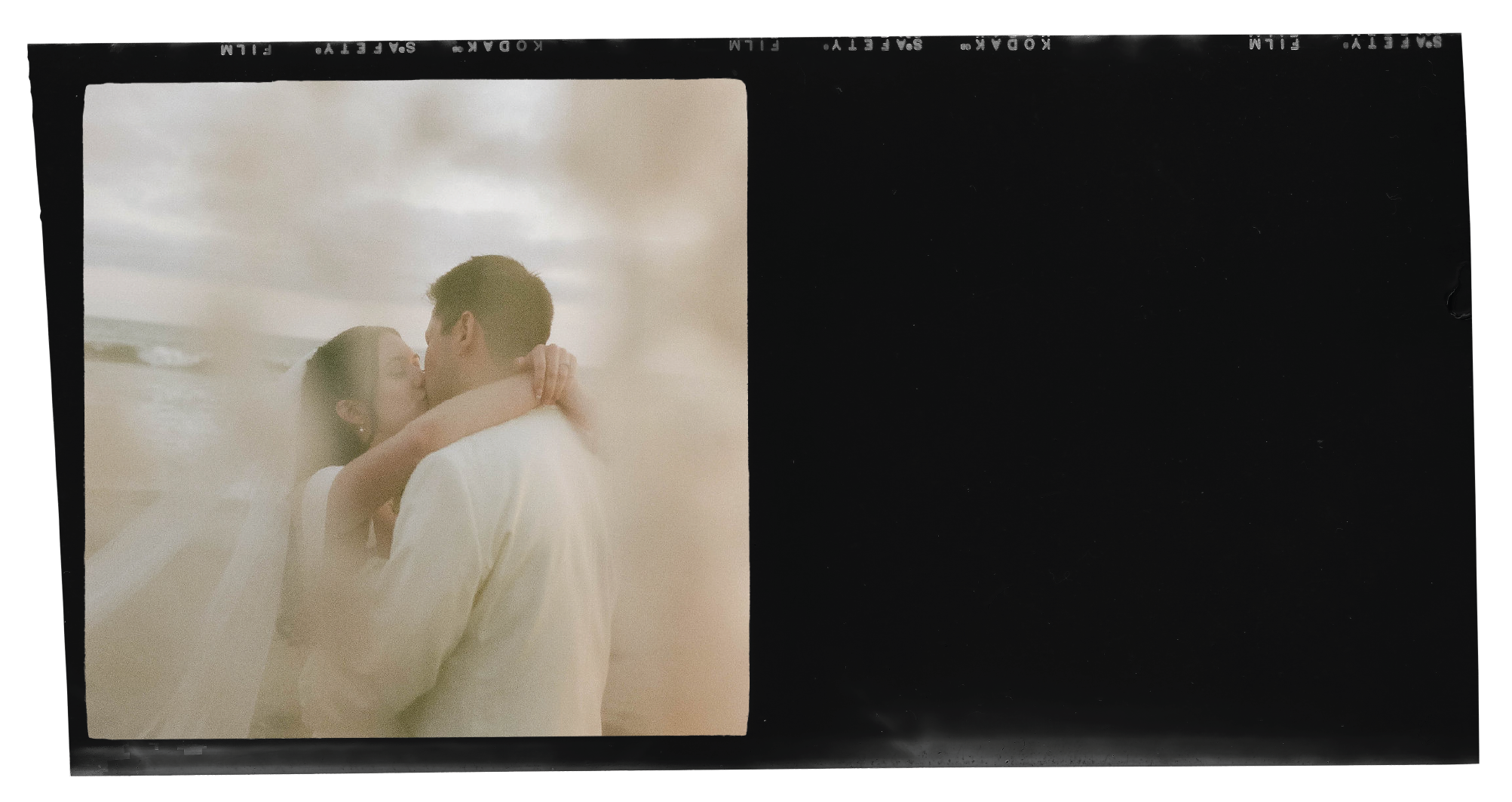 A couple sharing a kiss on the beach with clouds overhead, viewed through vintage film negatives.