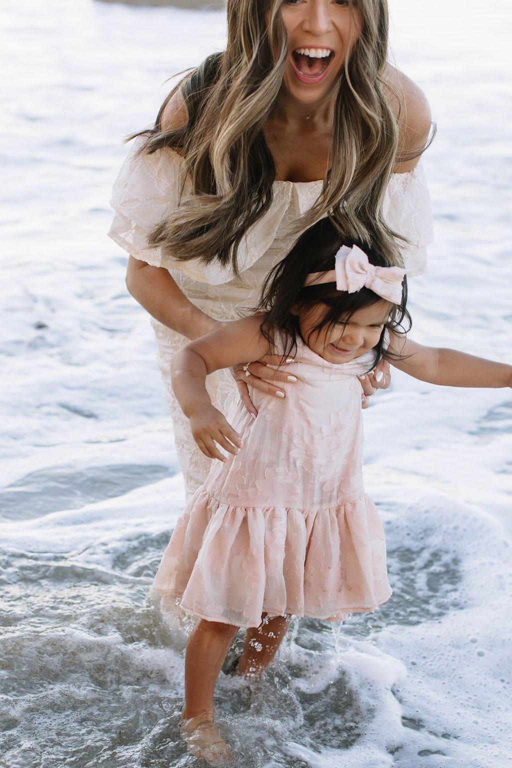 A woman and a young girl enjoying time in the ocean, with the woman holding the girl from behind while they stand in the water.