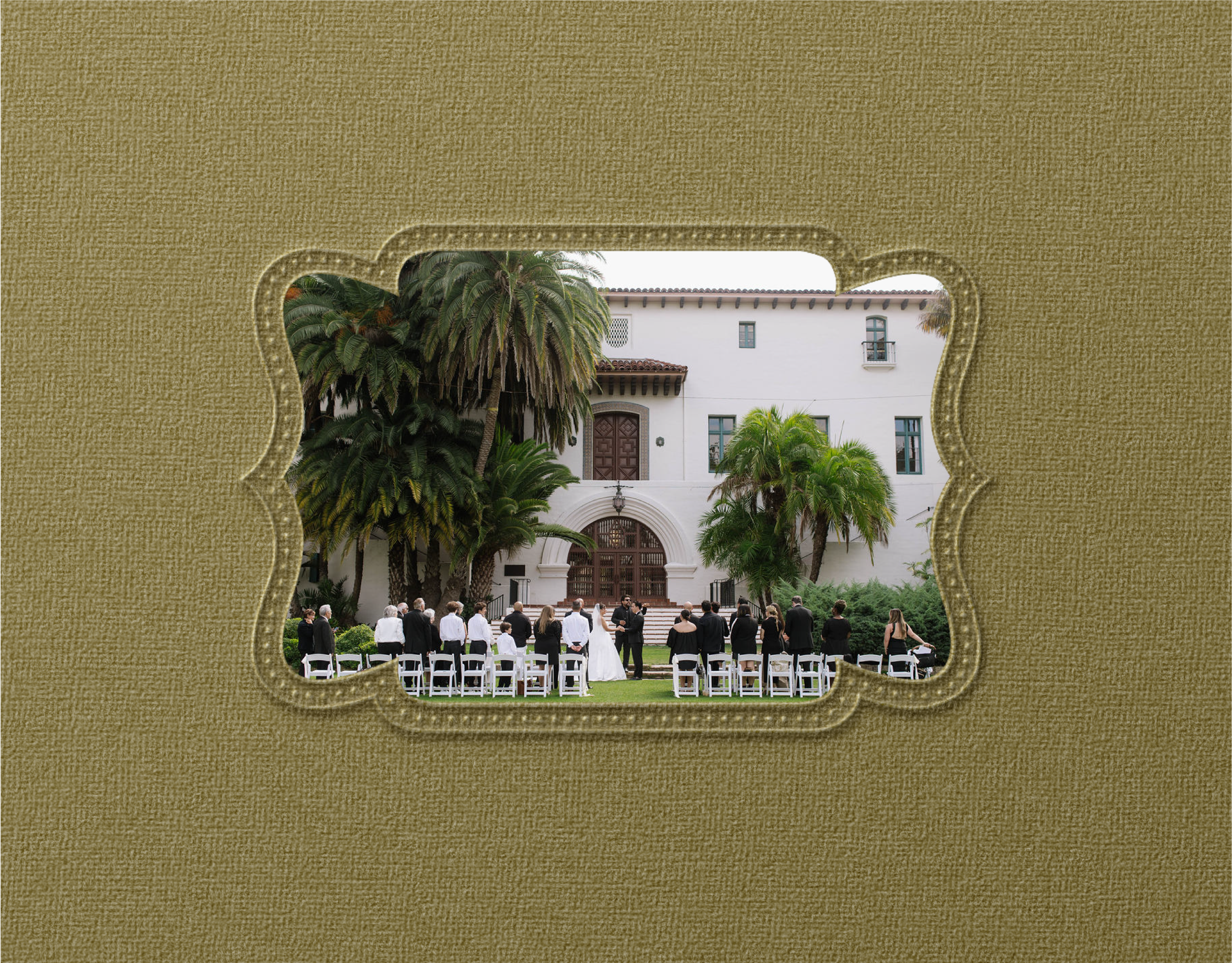 View through a decorative window frame showing a wedding ceremony outside a white building with palm trees, with guests seated on white chairs.