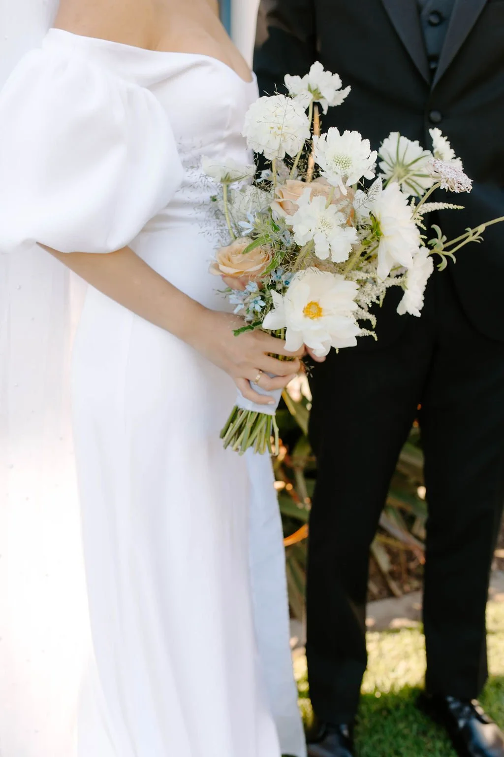 A bride and groom holding a bouquet of white and light pink flowers at their wedding.