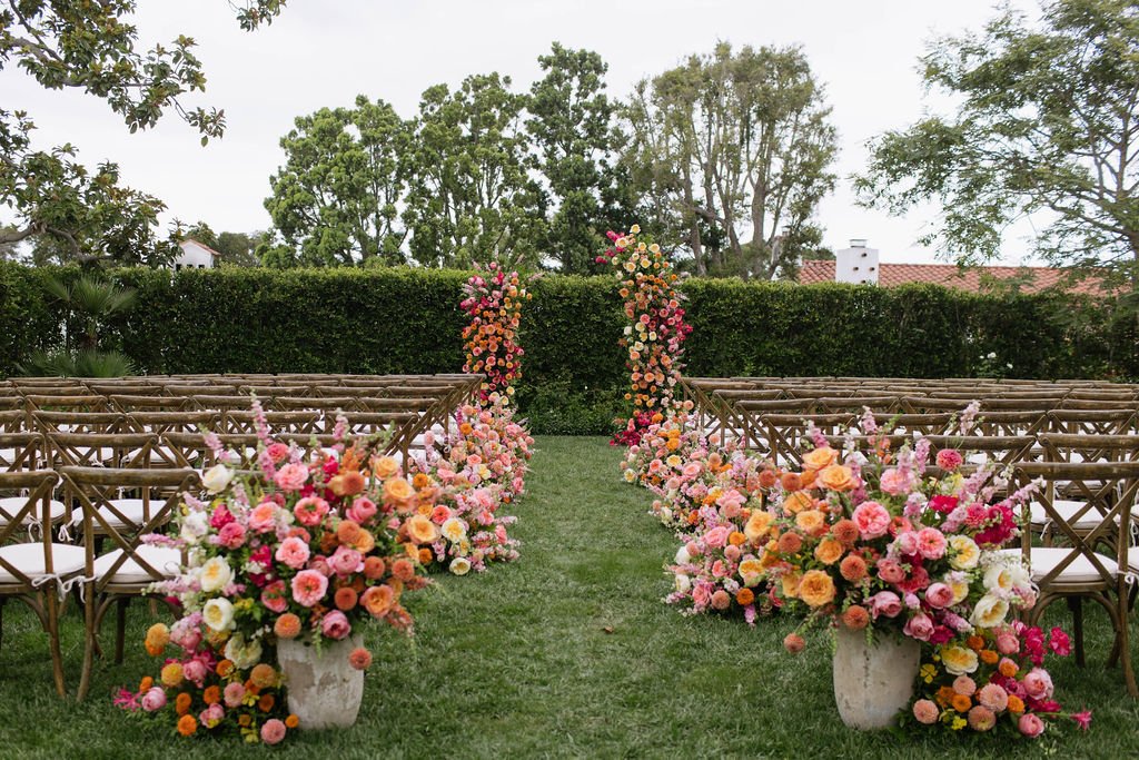 Outdoor wedding ceremony setup with floral arrangements and wooden chairs on a grassy lawn.