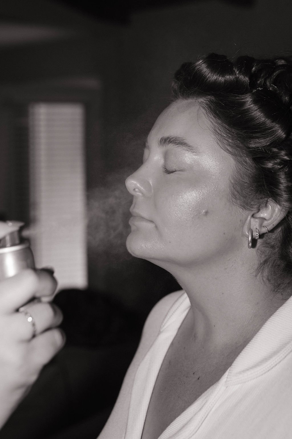 A woman with styled hair getting a facial spray from a person holding a spray can.