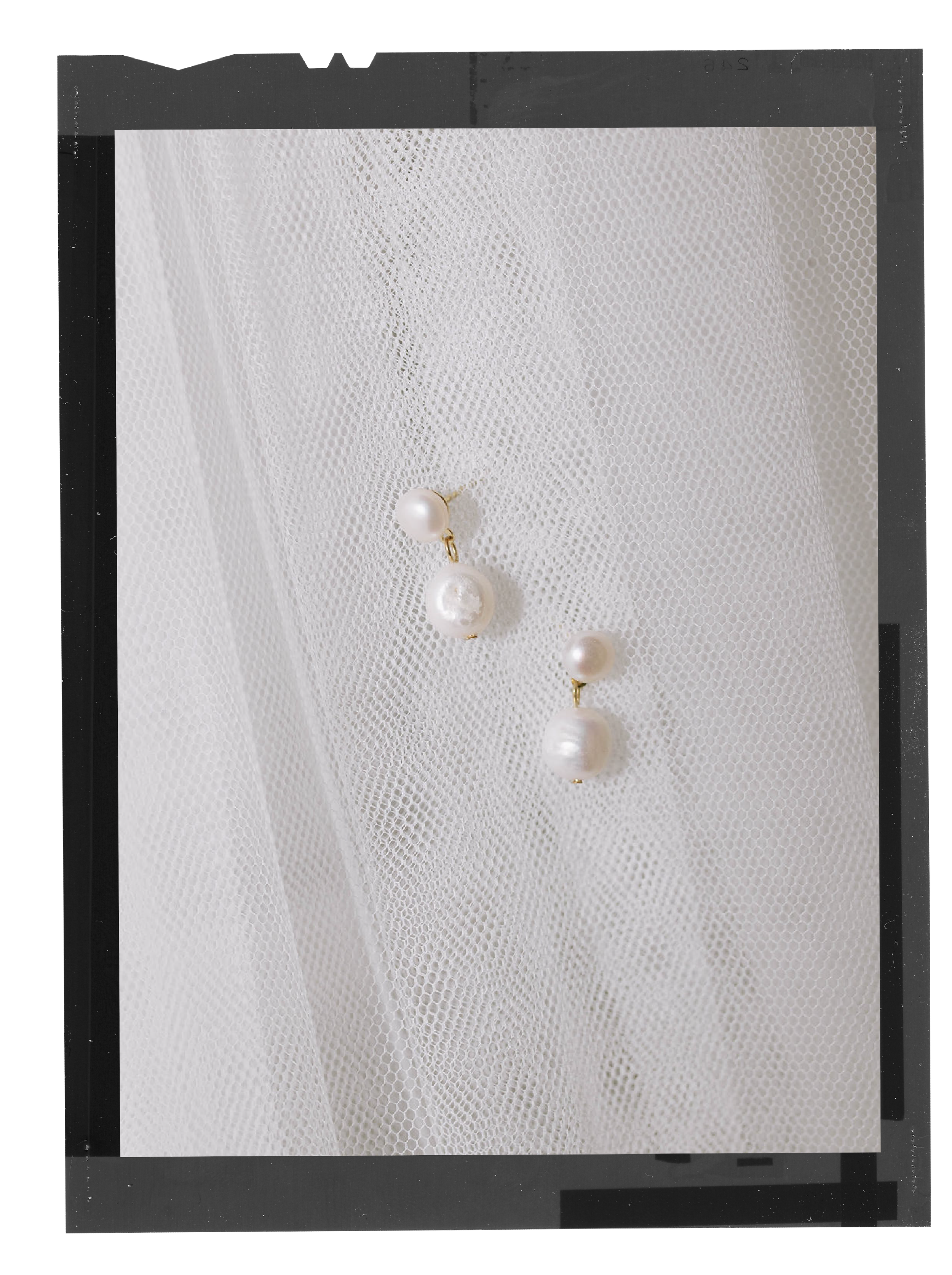 Pair of pearl drop earrings on textured white fabric background.