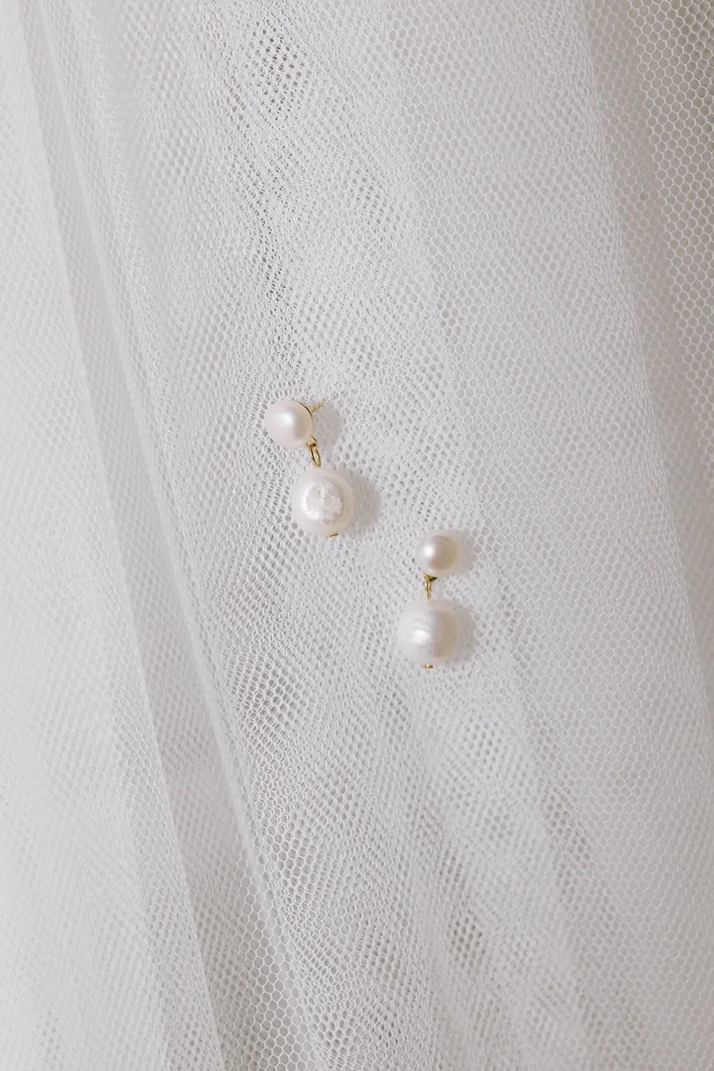Pearl earrings on white mesh fabric background.