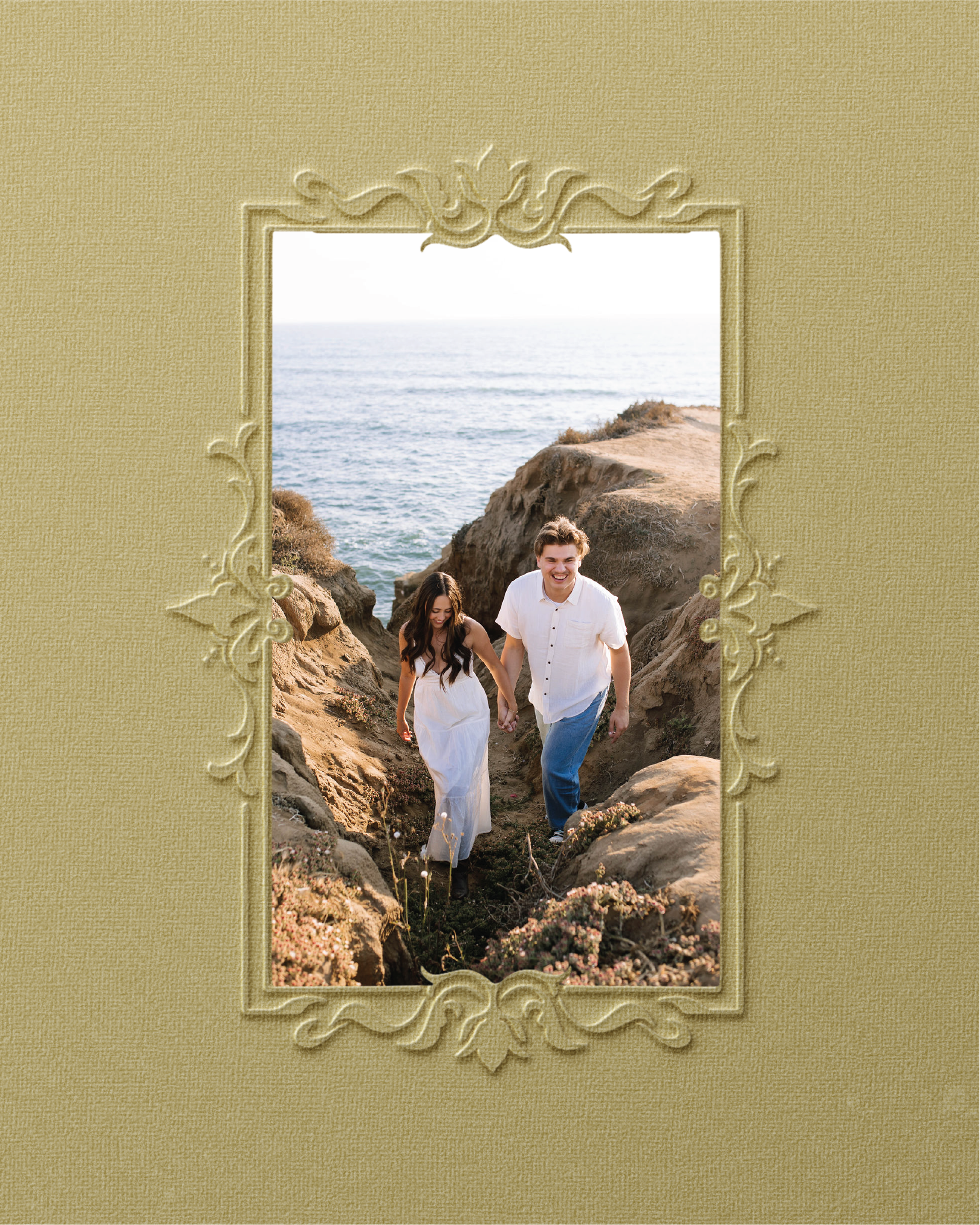 A couple walking in a rocky area near the ocean, framed by a decorative picture frame on a textured yellow wall.