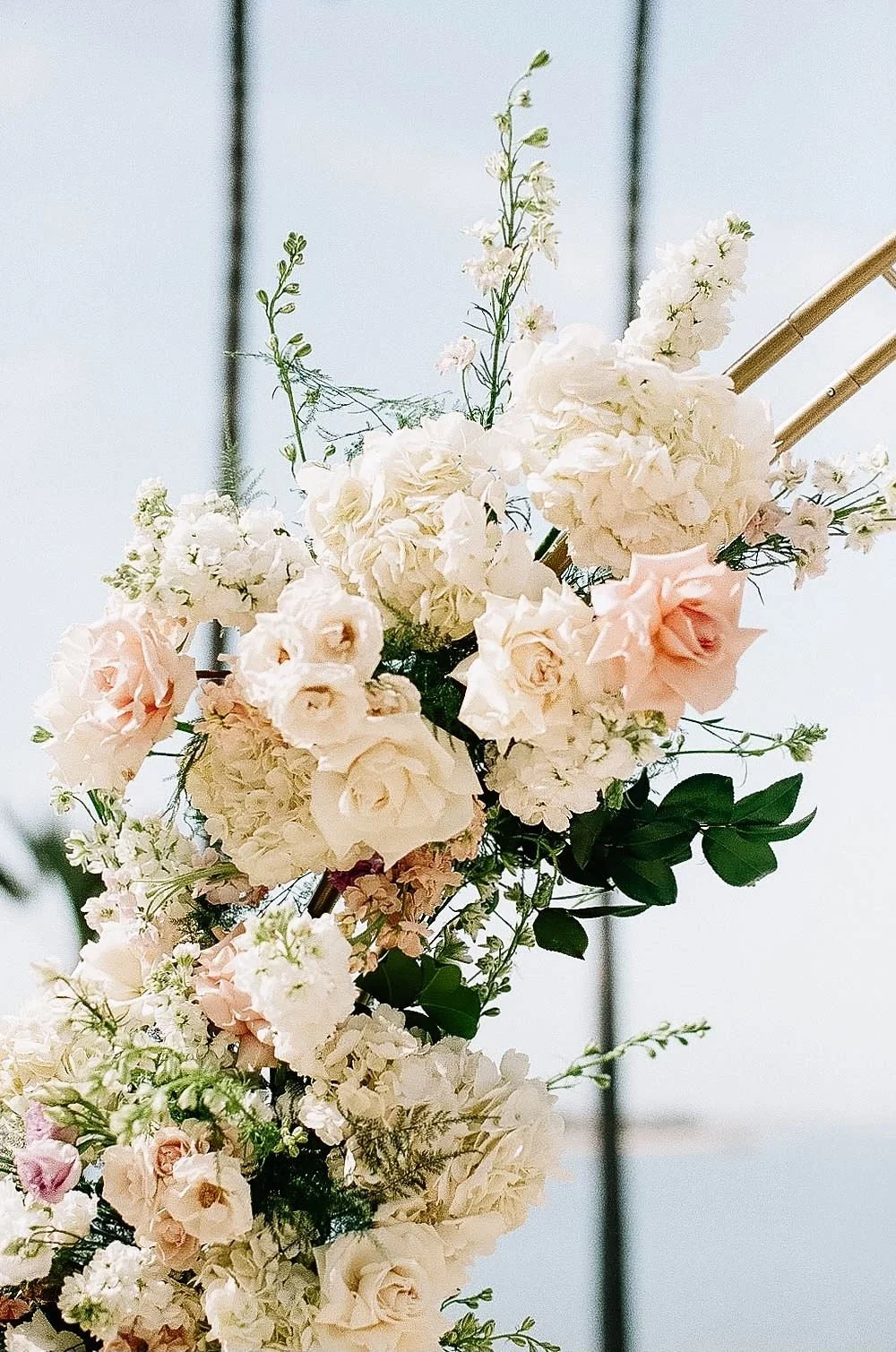 A wedding bouquet with white and light pink roses, hydrangeas, and green foliage, held by a person in a sleeveless dress.
