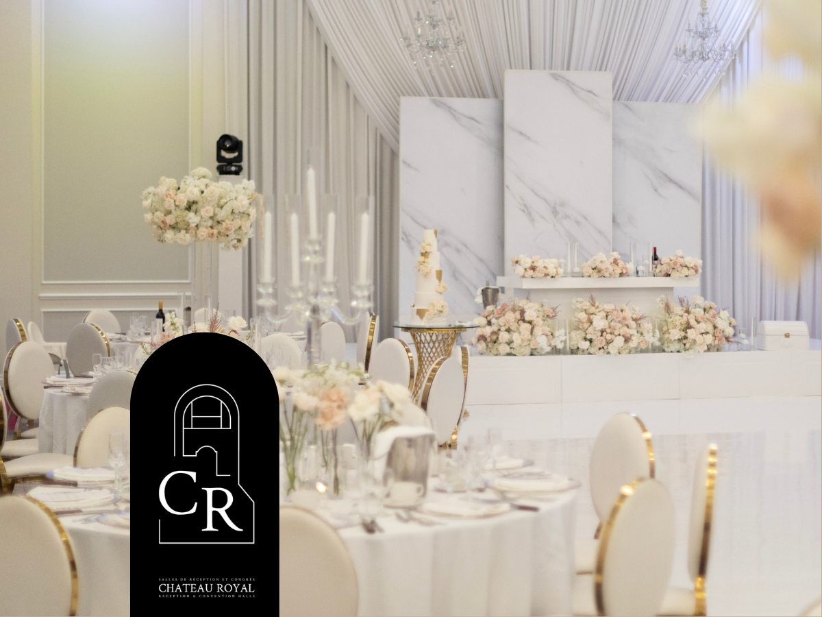 Salle de réception élégante avec des tables rondes, des décorations florales en pastel, un gâteau de mariage et un fond en marbre blanc.