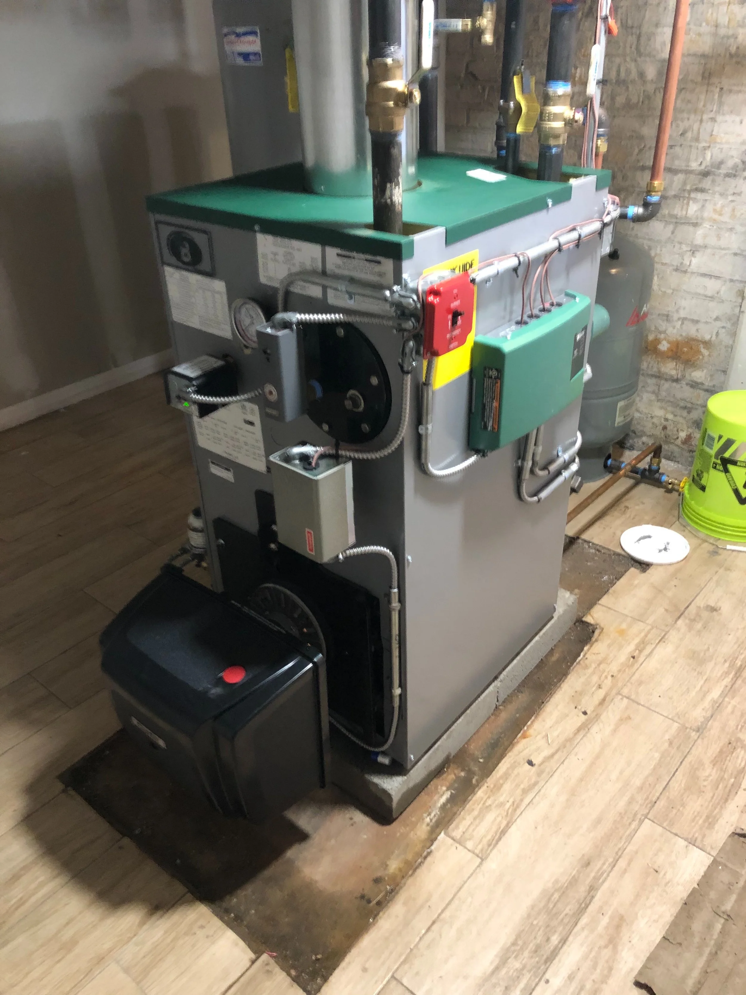 A furnace or boiler unit installed on a concrete pad in a basement or utility room, with pipes and control panels visible.