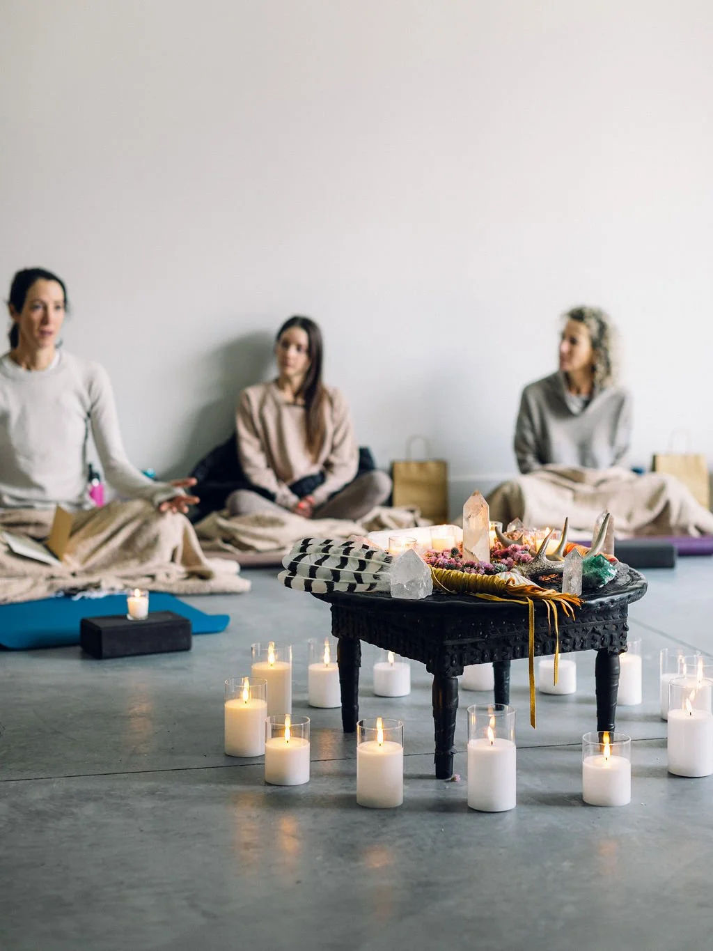 Women sitting on the floor in a circle around an altar with crystals, candles, and spiritual objects, participating in a meditation or spiritual ceremony.