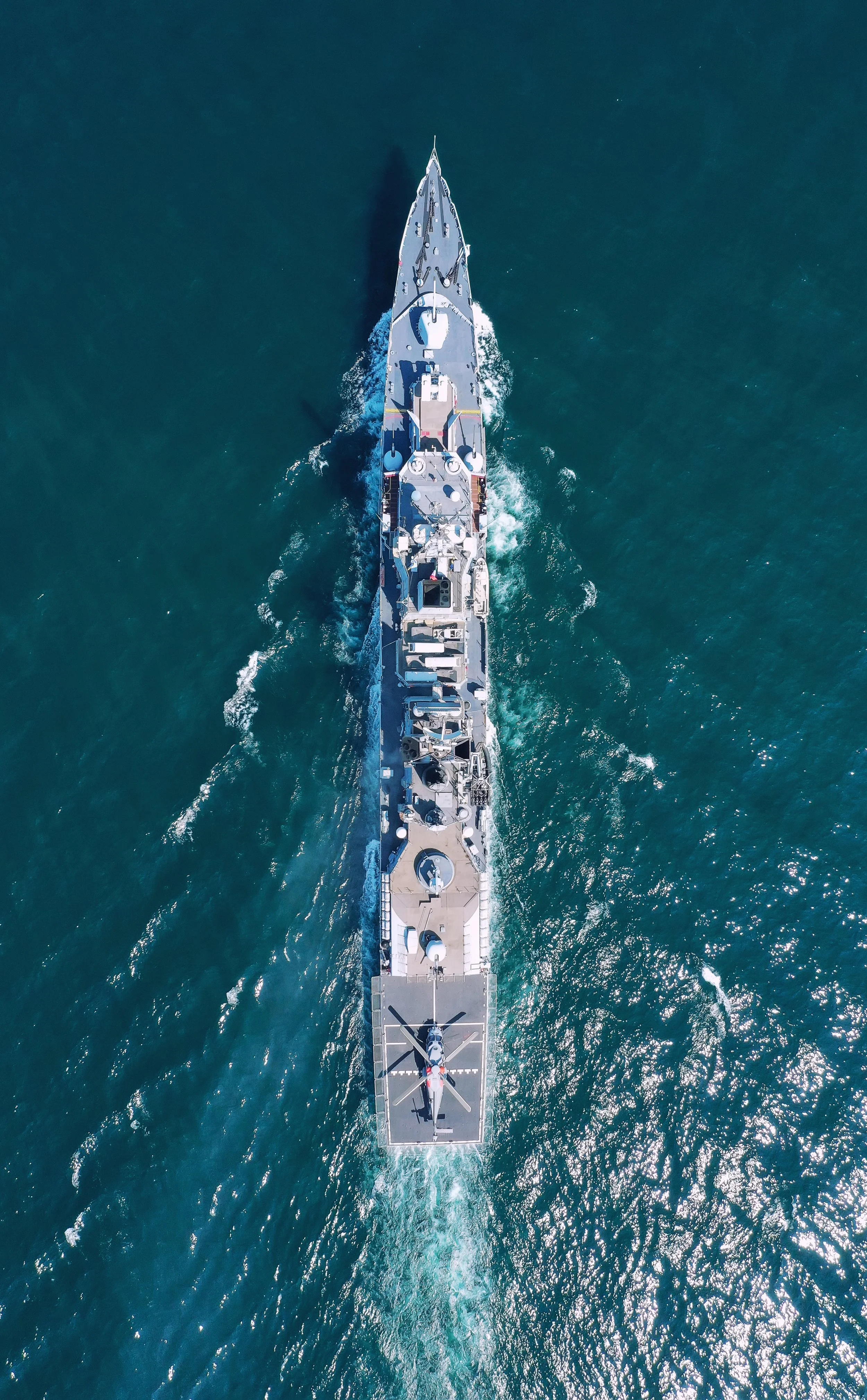 An aerial view of a large naval ship, seen from above, moving through the ocean.