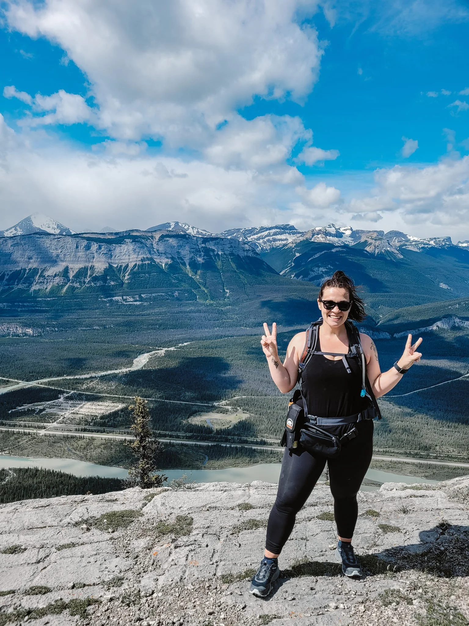 Woman standing at the peak of top of a mountain giving peace fingers