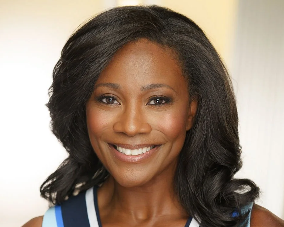 A smiling woman with dark hair styled in loose waves, wearing a blue dress.