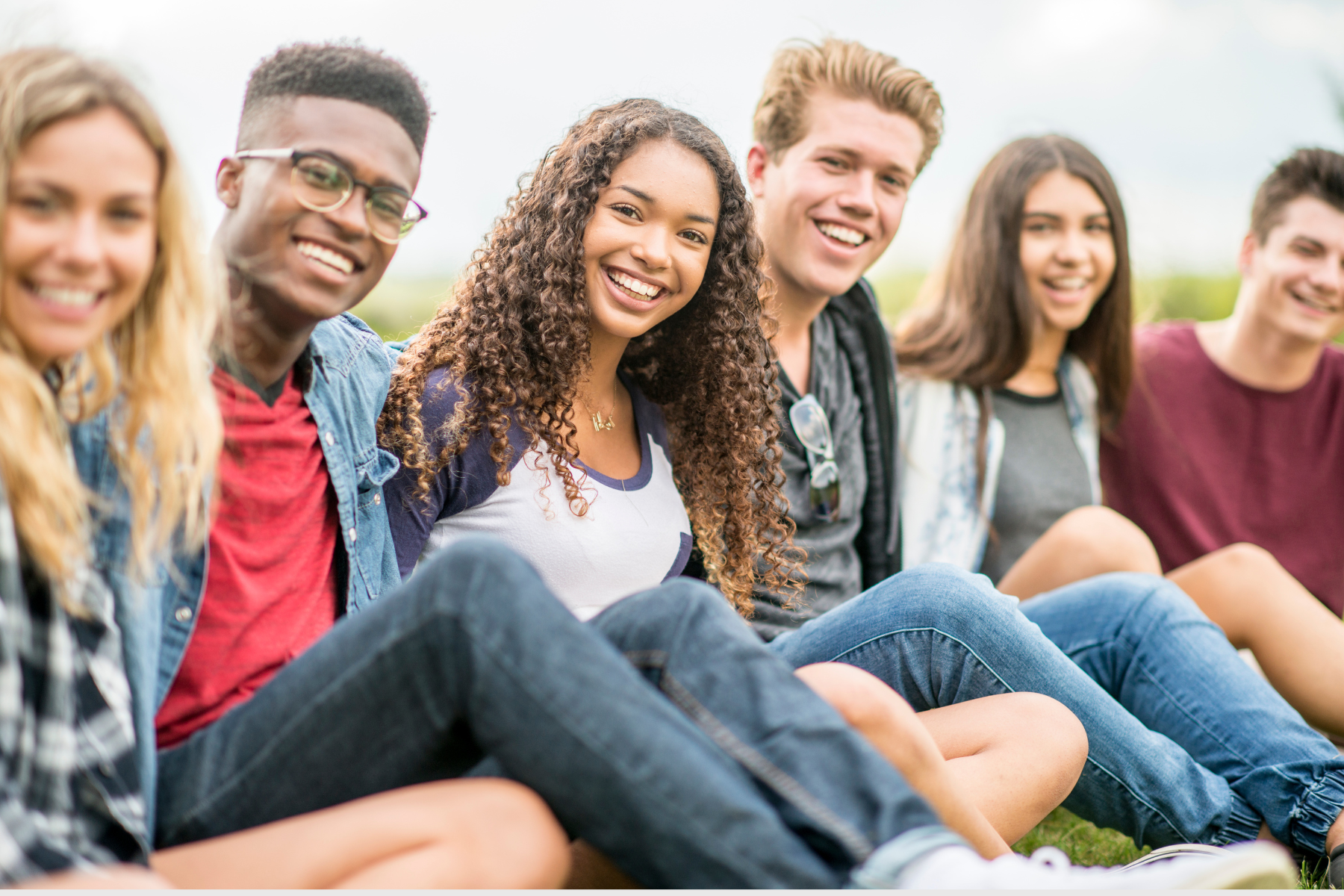 Group of diverse young friends sitting on grass outdoors, smiling and enjoying each other's company.