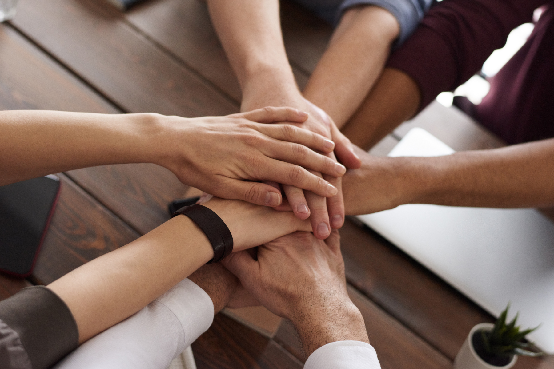 Group of diverse people stacking their hands together on a wooden table in a show of unity.