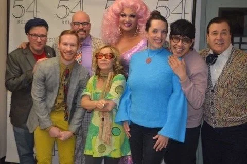 Group of eight people, including Drag Queen in pink wig, posing together at a Belmond event, smiling for the camera.