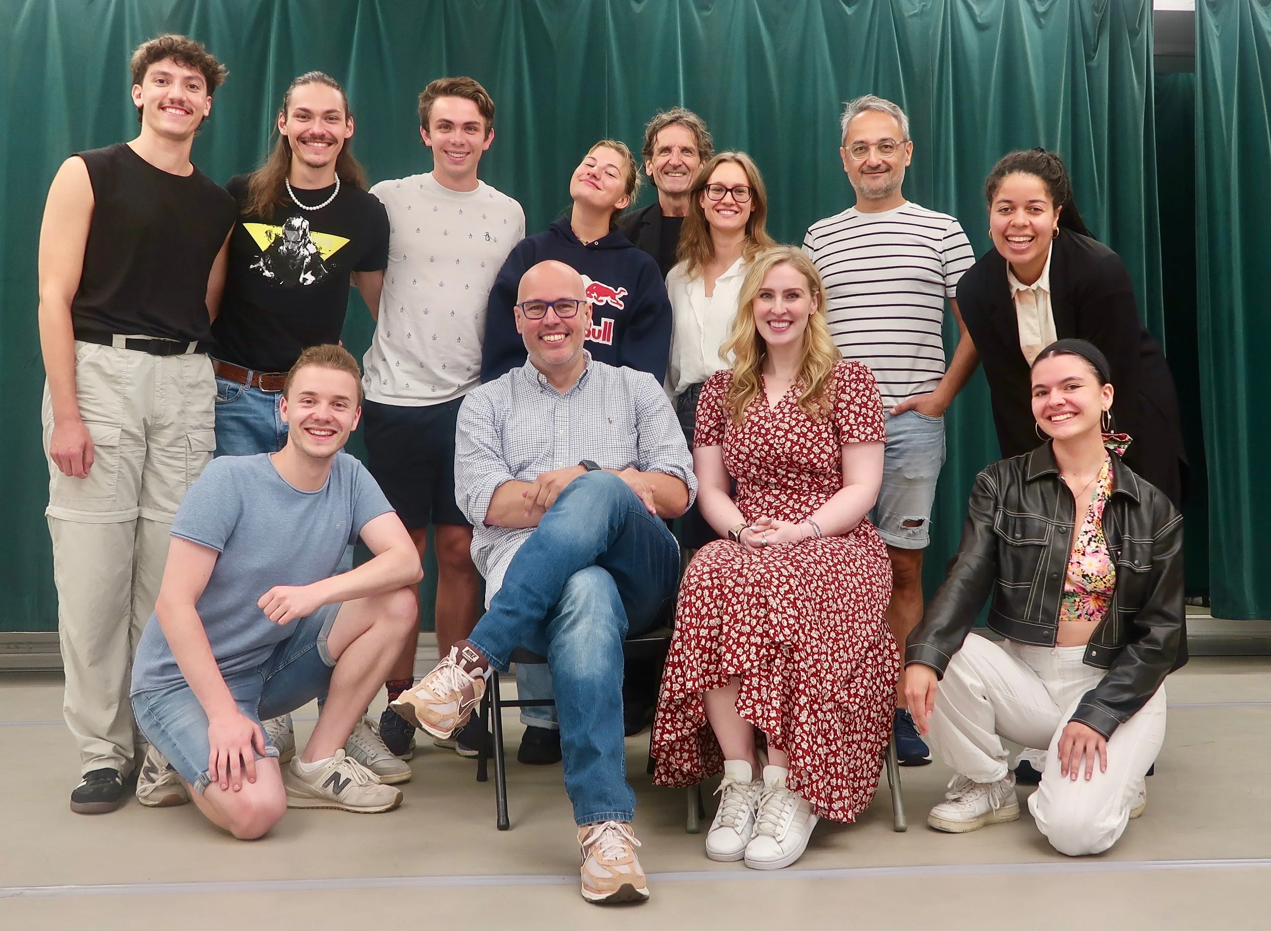 Group of people posing for a photo in front of green curtains, including men and women of various ages, some sitting and some standing. Robert W. Schneider.