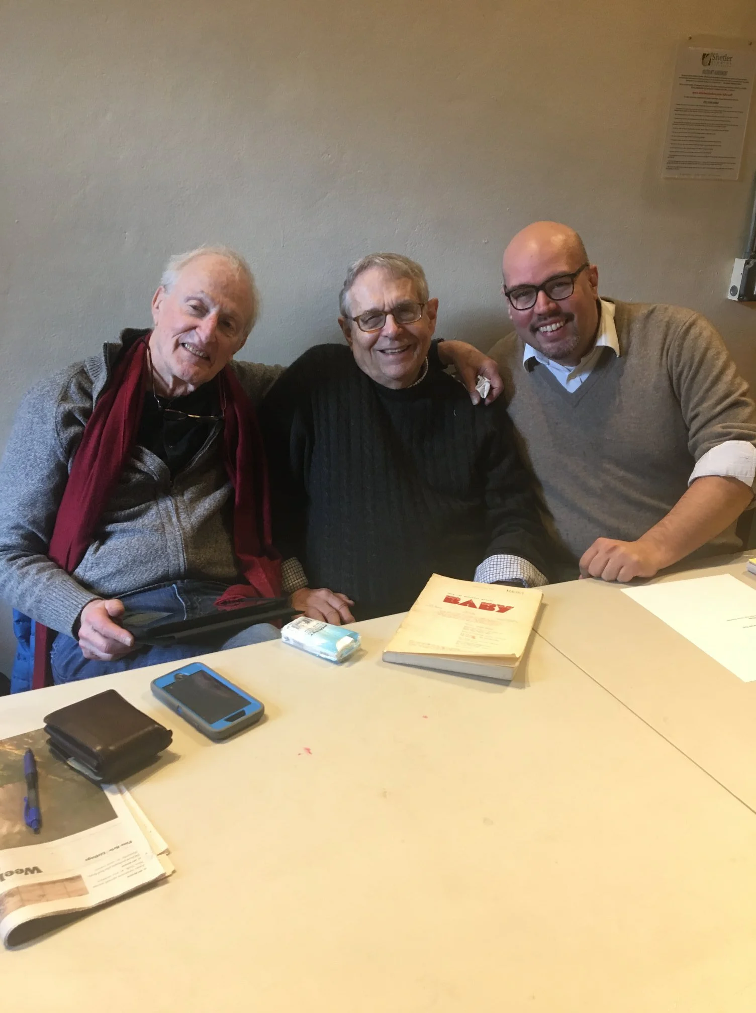 Three men sitting together at a table, smiling for the camera indoors.
