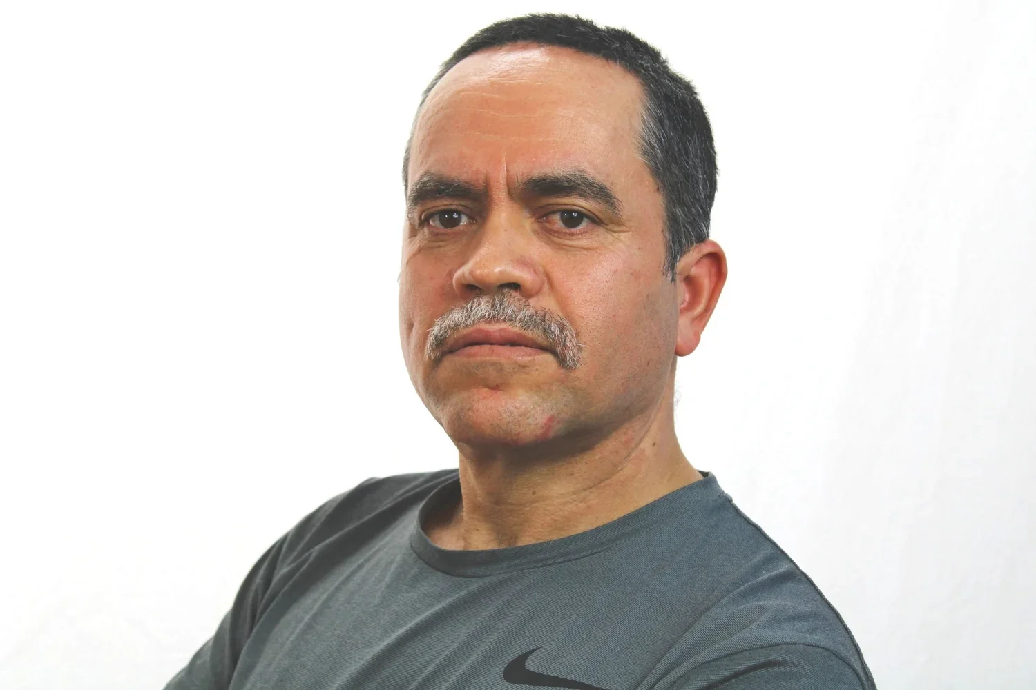 MLVS Team: Alfredo Rodrigues, Custodian. A man with short dark hair, a mustache, and a serious expression, wearing a gray Nike shirt, standing against a white background.