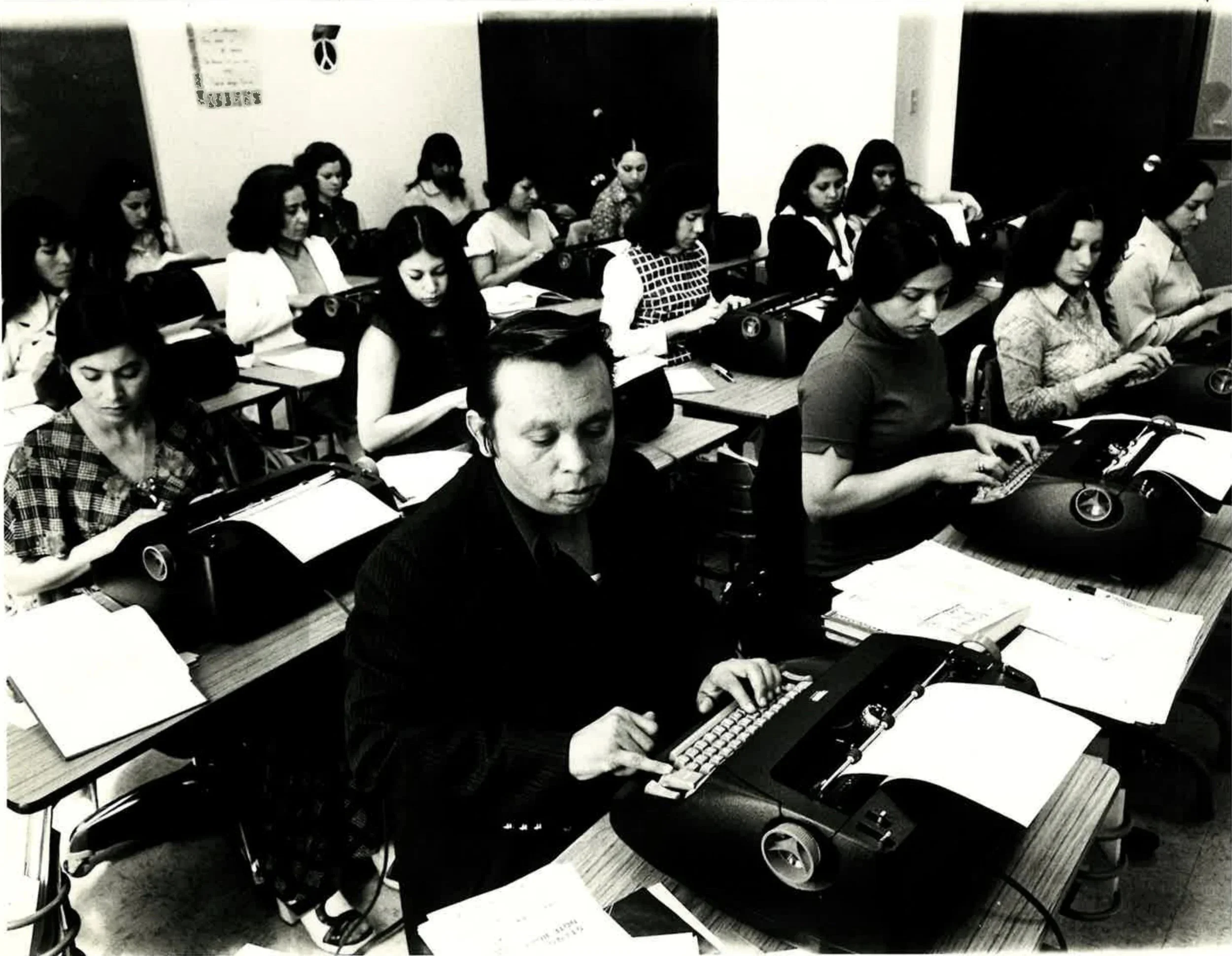 MLVS History: A classroom filled with predominantly young women using vintage typewriters at desks, with one older woman in the foreground.