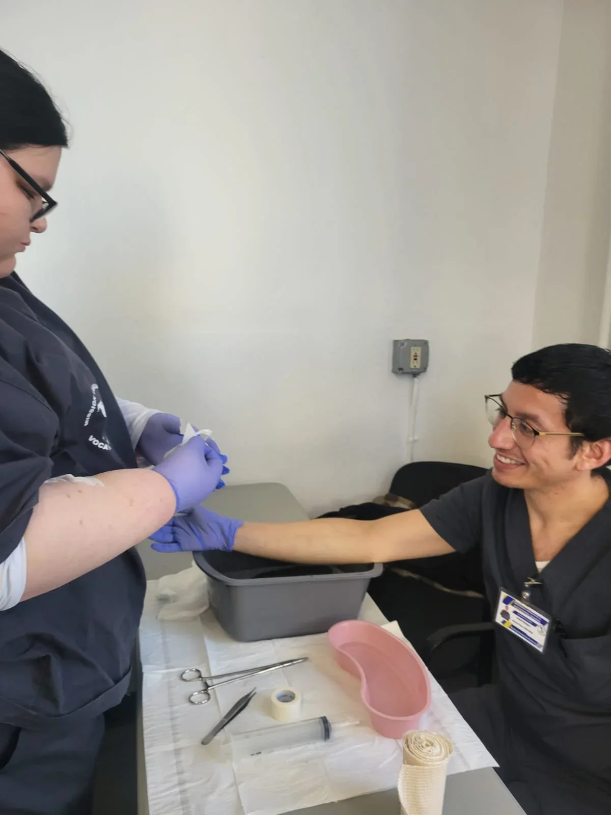 MLVS Medical Assistant Program: A healthcare worker is extracting blood from a smiling patient's arm in a clinical setting, with medical supplies on the table.
