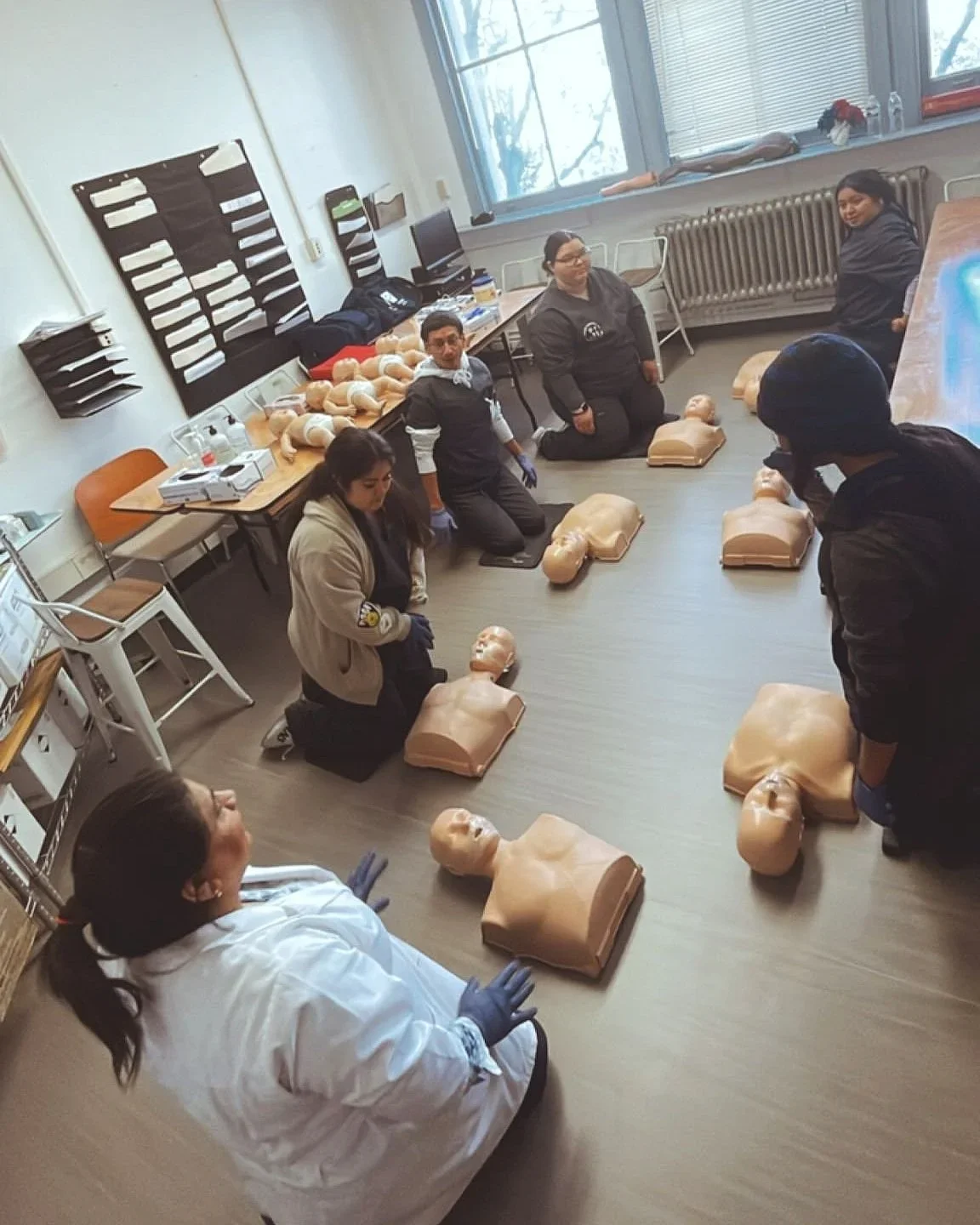 MLVS Medical Assistant Program: Group of people participating in CPR training with manikins in a classroom.