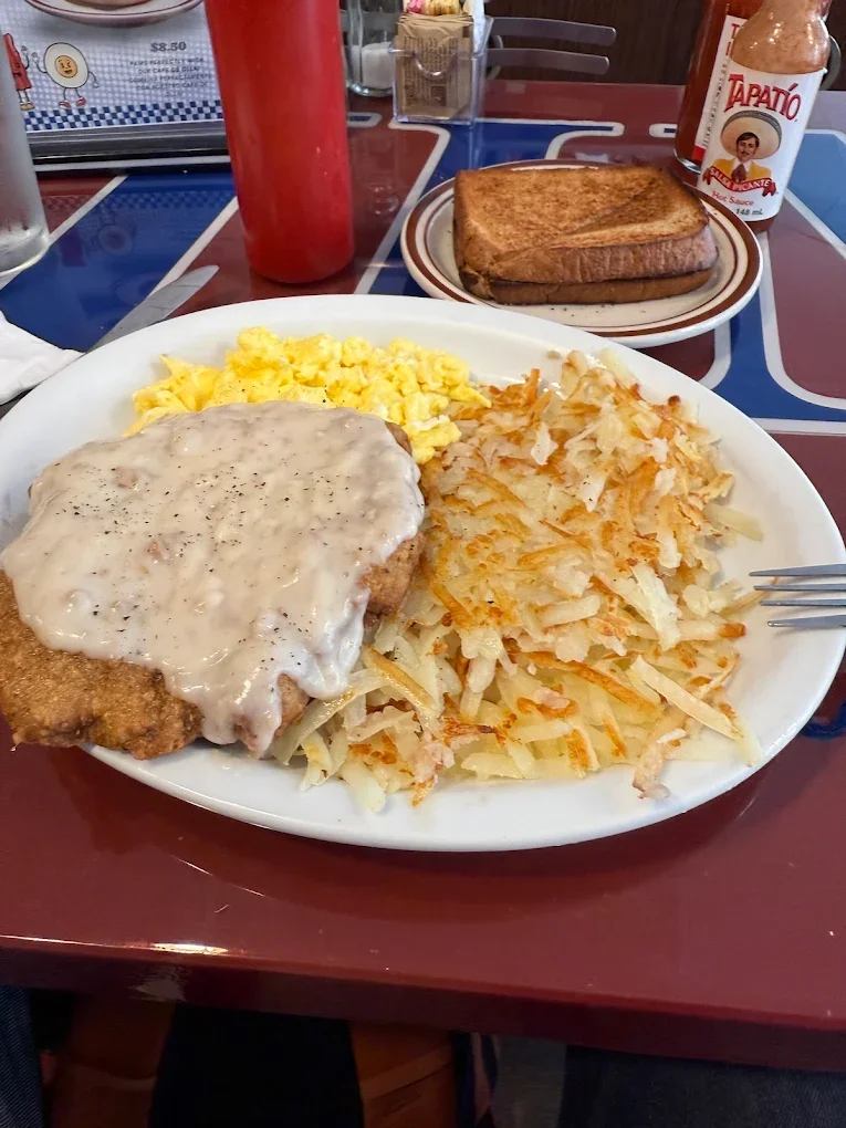 Jims By MLVS: Chicken Fried Steak and two eggs. Breakfast with scrambled eggs, hash browns, chicken fried steak with gravy, toast, and condiments on the table.