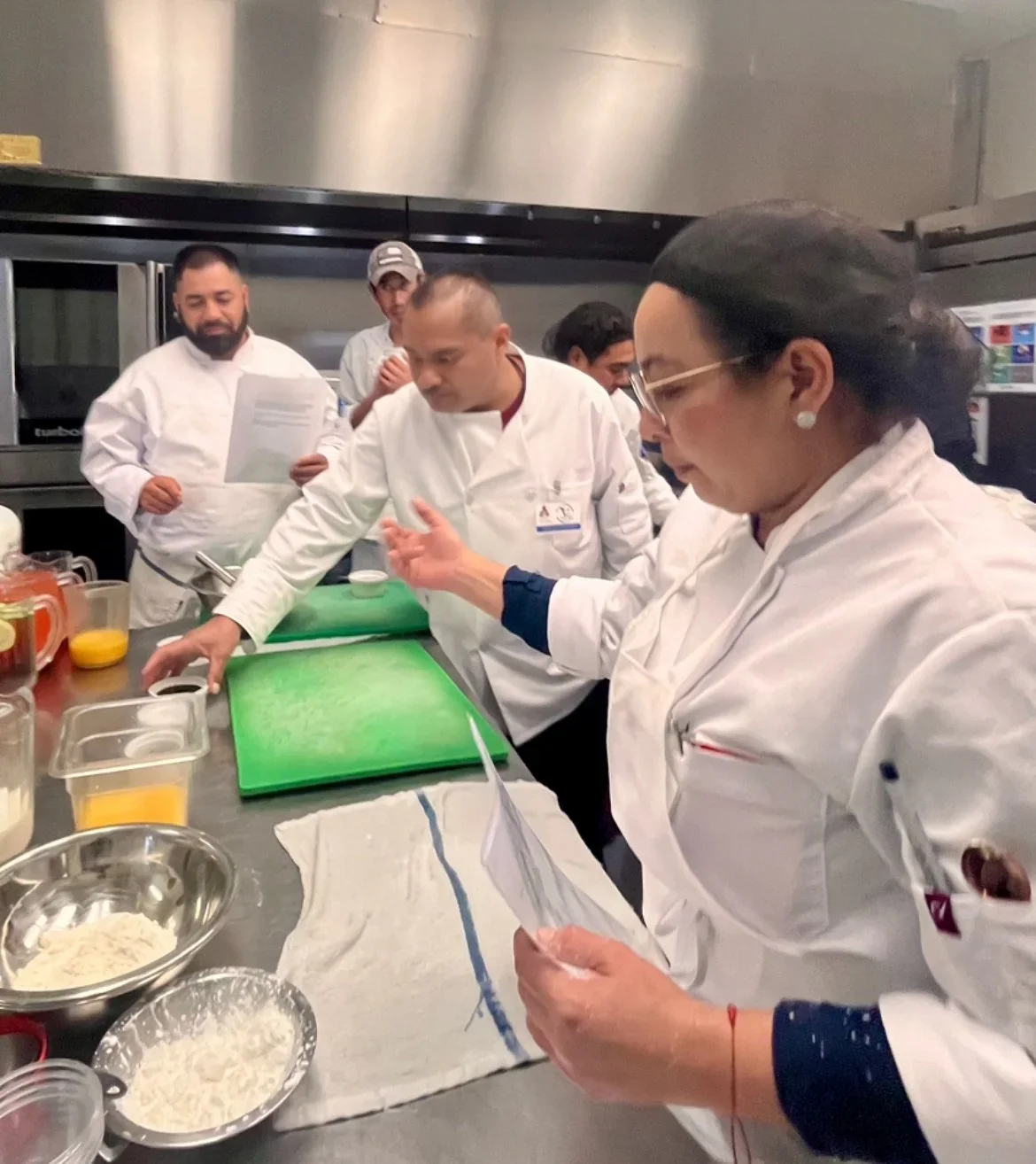 MLVS Culinary Arts Program. Group of chefs in a professional kitchen, focused on preparing a dish, with various ingredients and utensils on the counter.