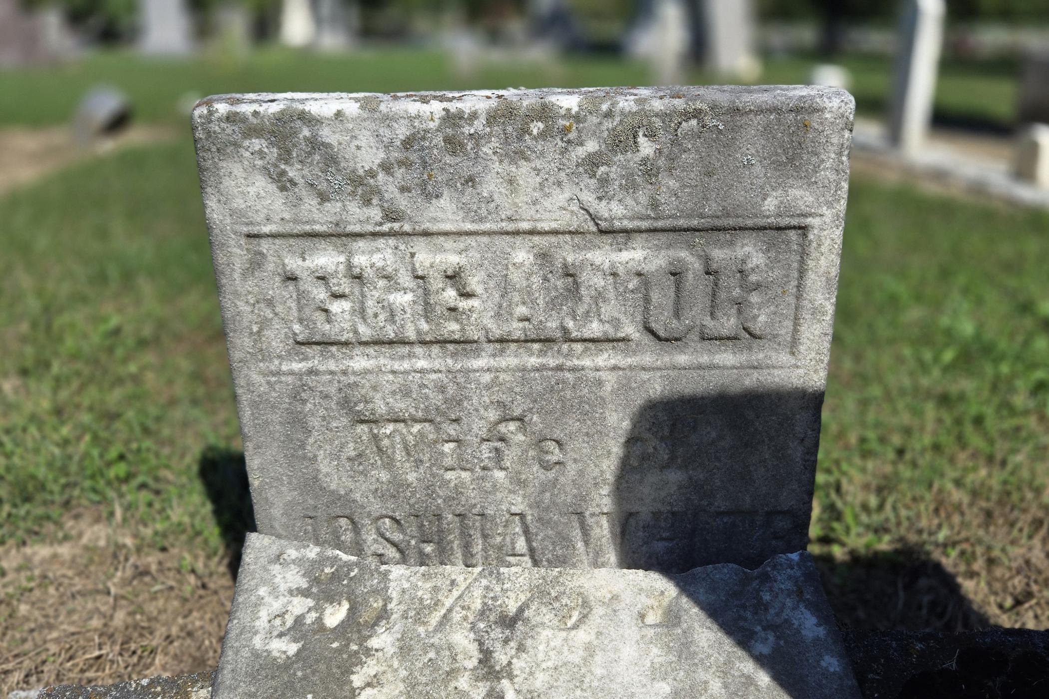 Close view of a weathered gravestone reading "Eleanor, wife of Joshua White," its lower part broken away.