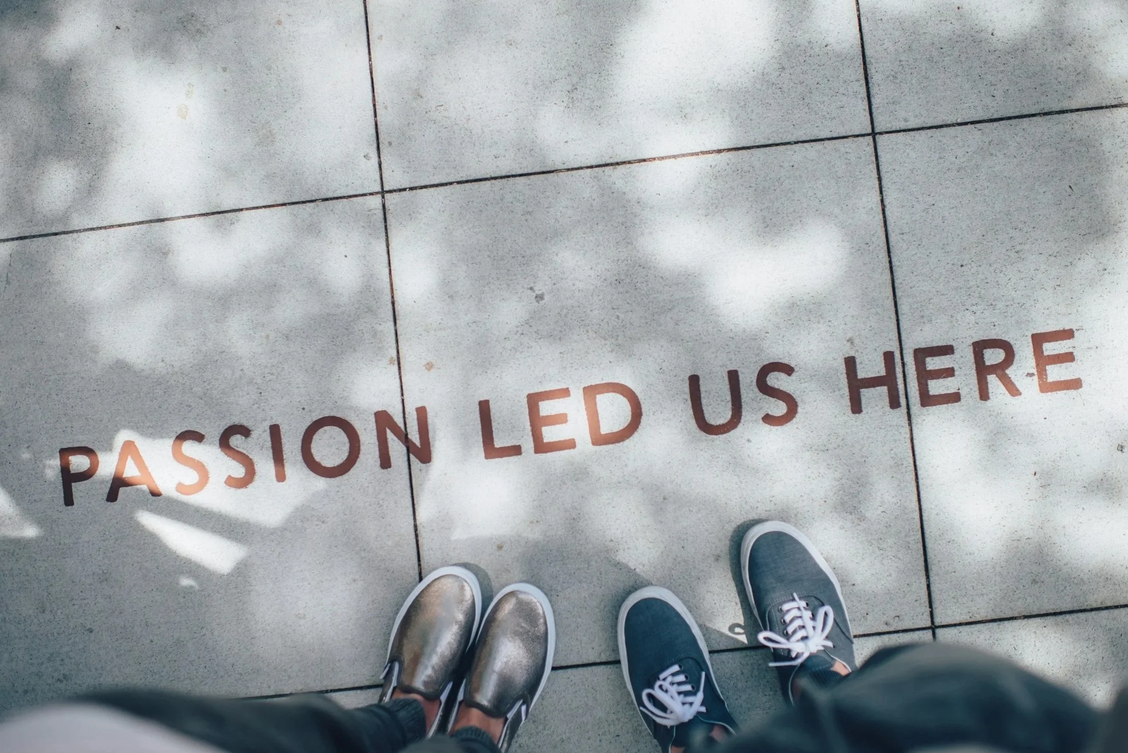 People standing on a sidewalk with the words "PASSION LED US HERE" written on the ground.