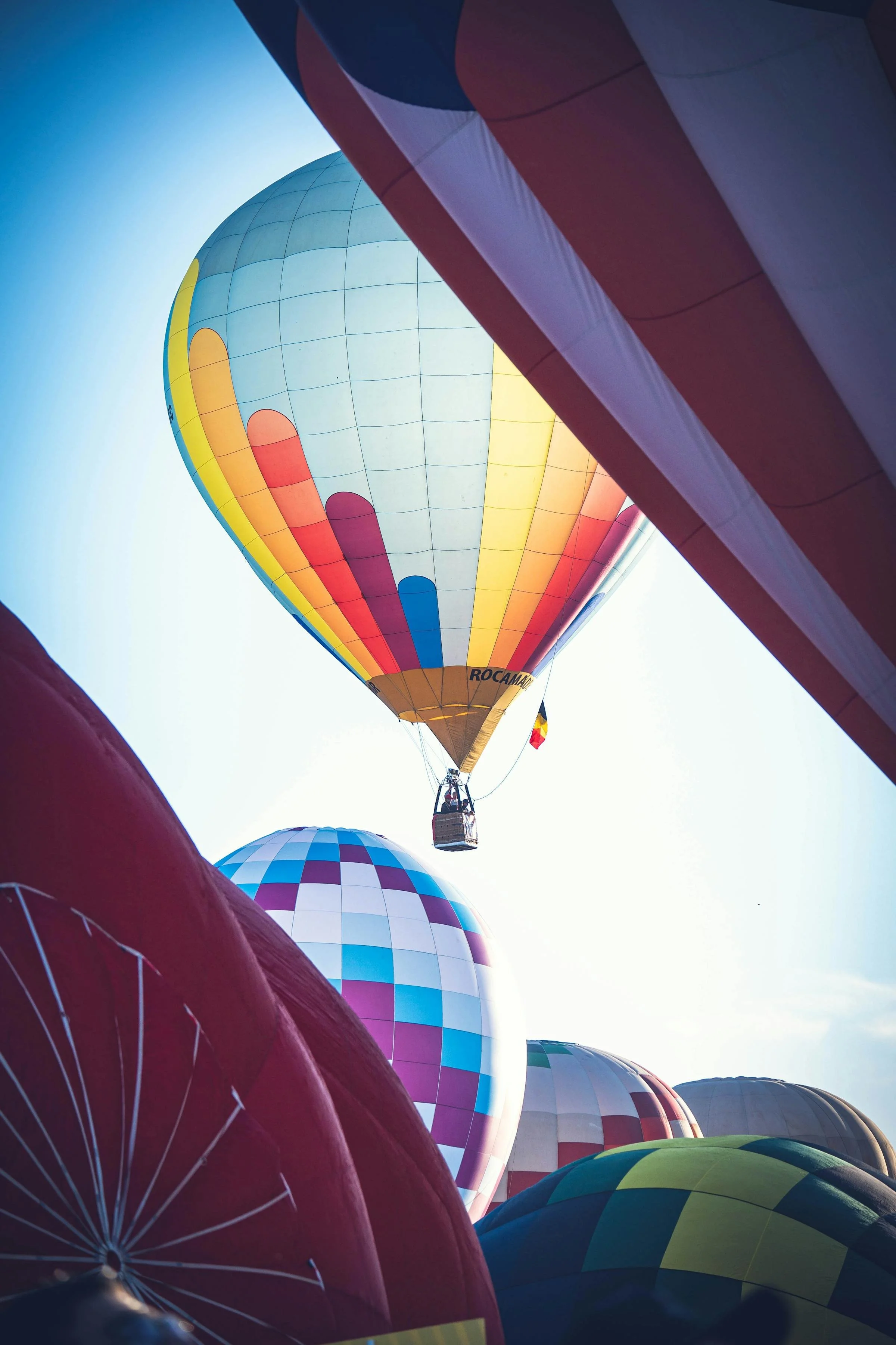 Colorful hot air balloons in flight with one balloon prominently rising in the background and several others resting on the ground.