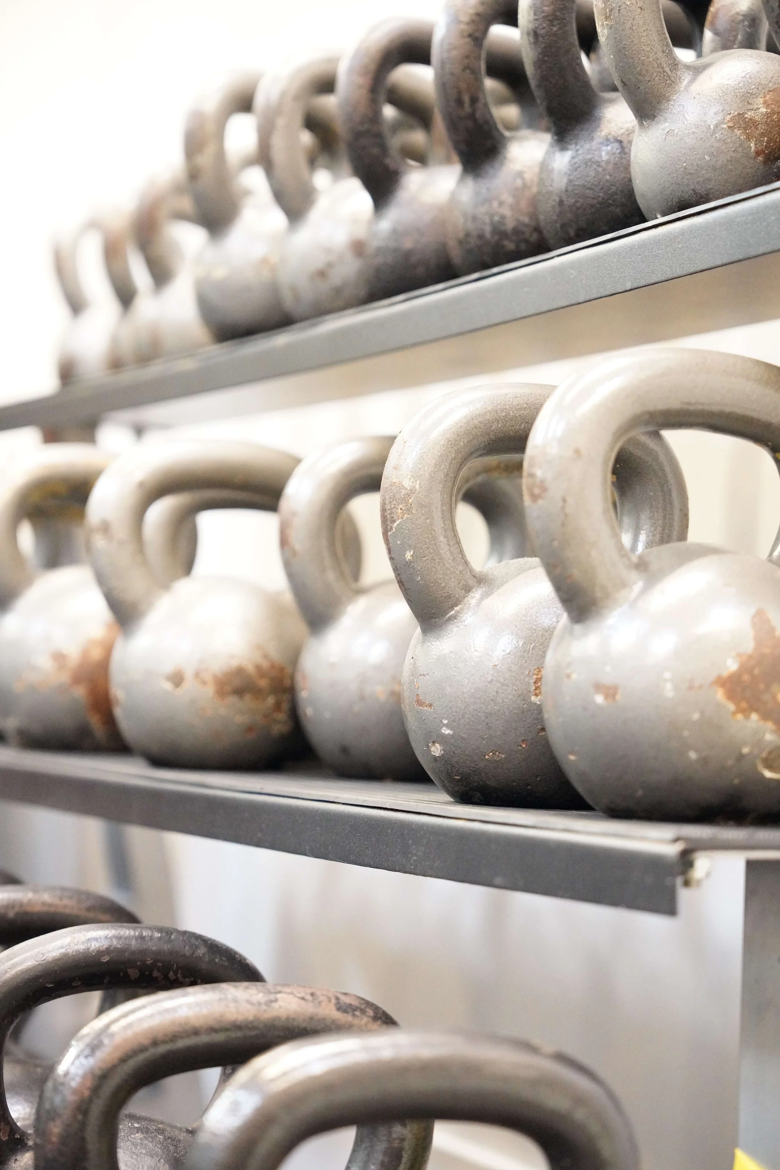 Multiple metal kettlebells on a shelf, some showing rust and signs of wear.
