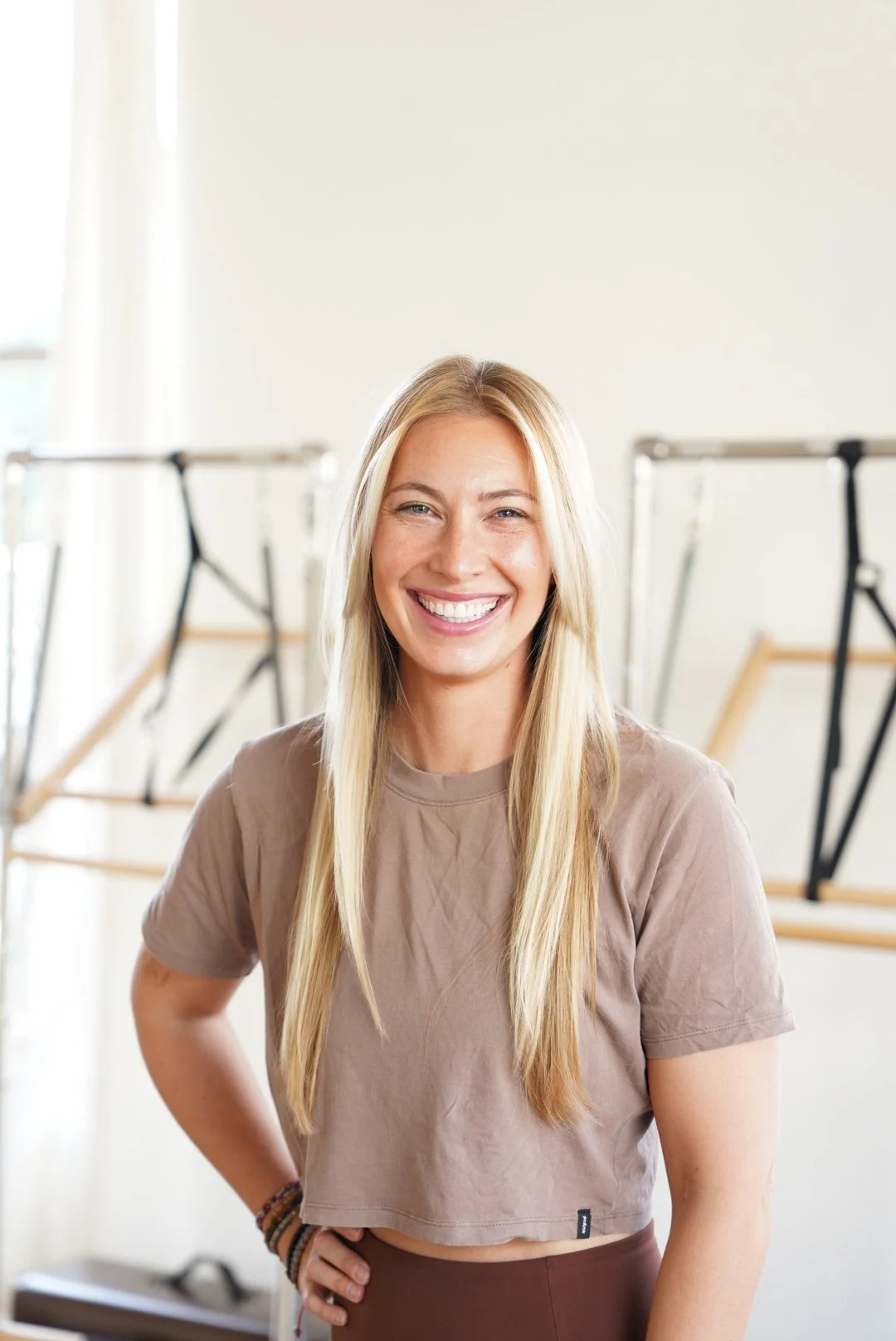 A smiling blonde woman wearing a beige cropped t-shirt in a dance studio.