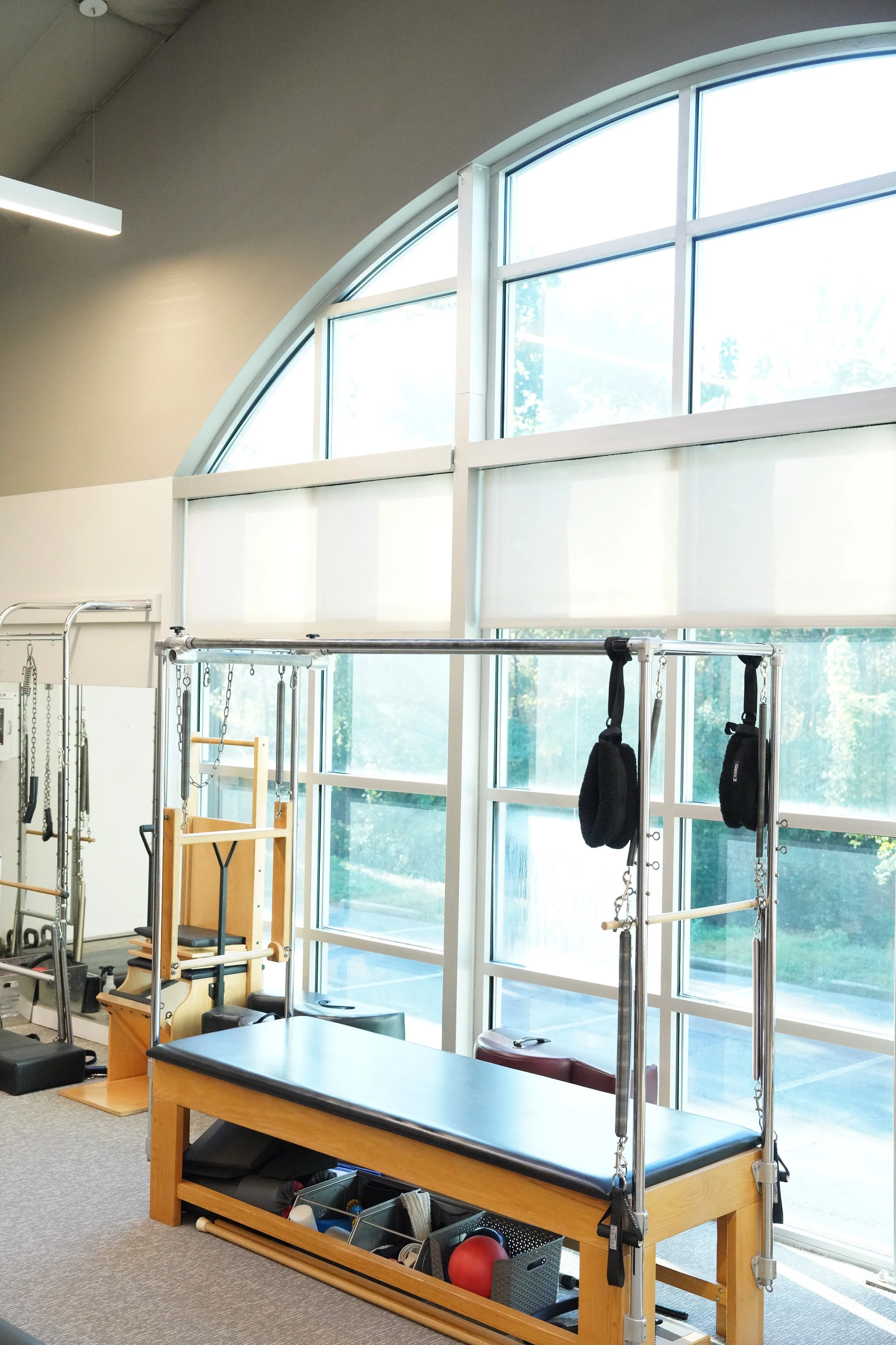 Inside a physical therapy or fitness clinic with rehabilitation equipment near large windows, including a wooden therapy table and resistance bands.