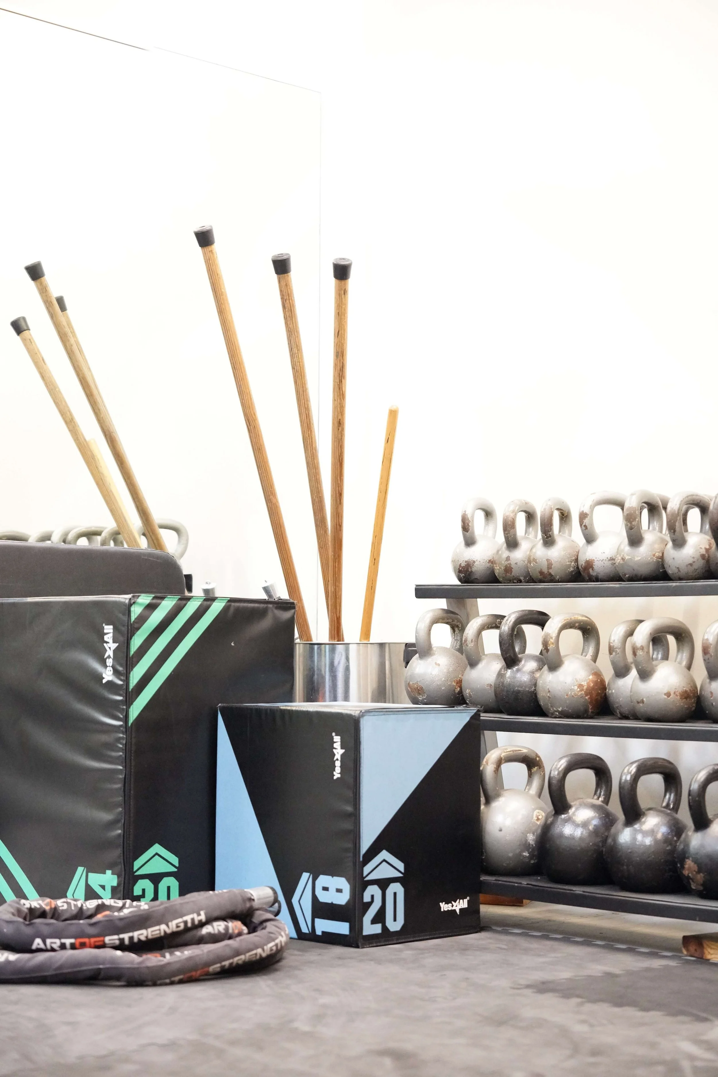 Gym equipment including wooden sticks, kettlebells, and plyometric boxes in a fitness training area.